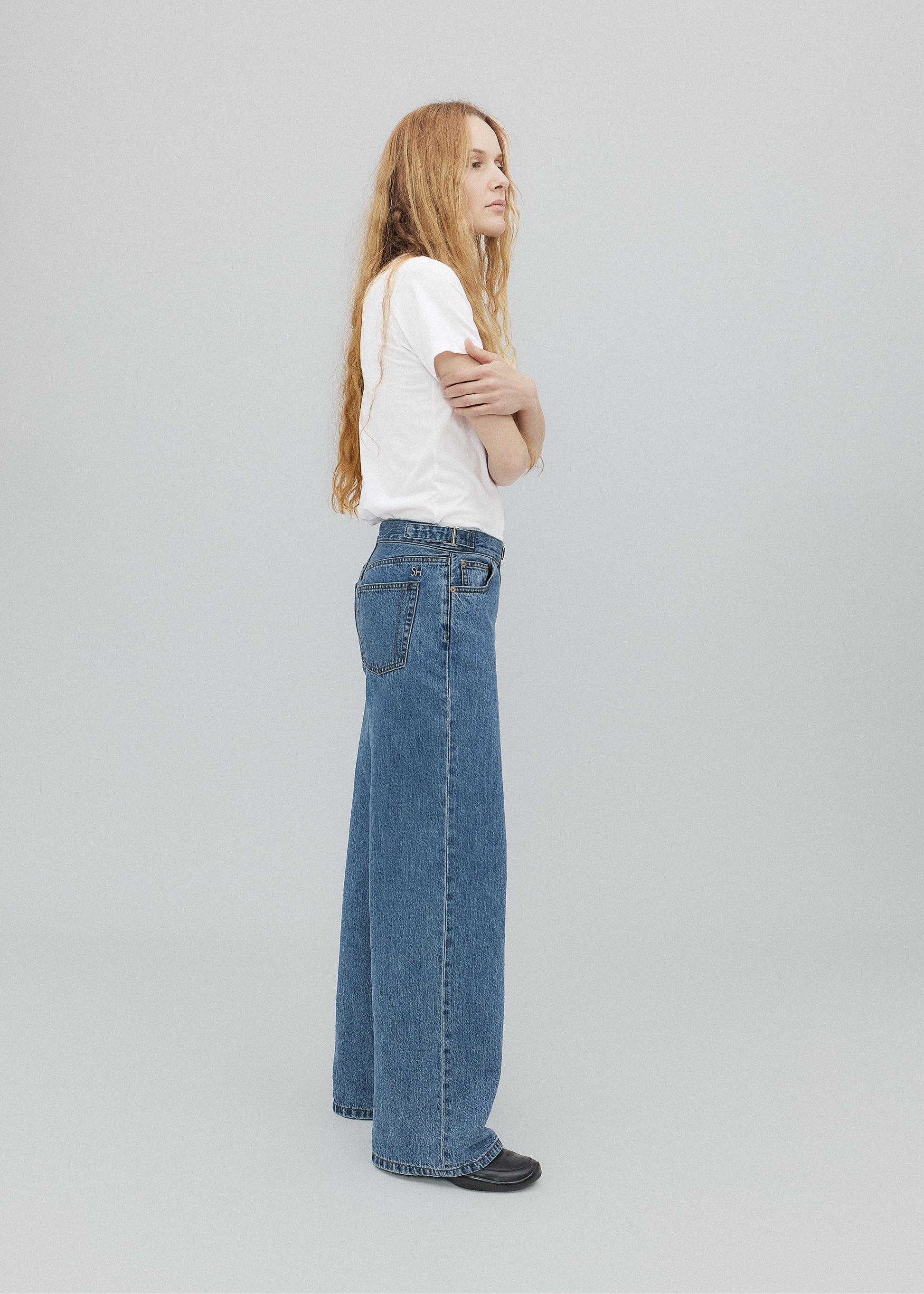 Woman wearing blue jeans and a white shirt on a light gray background