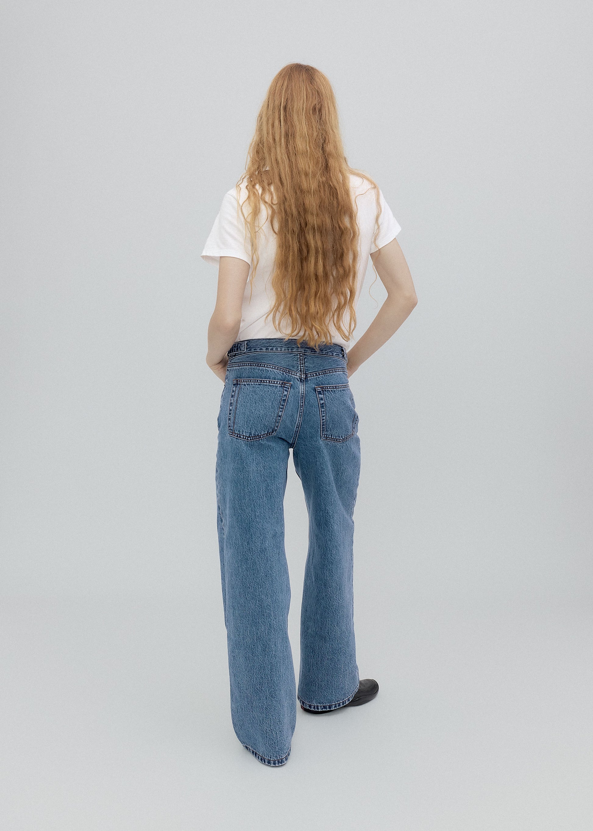 Person wearing blue jeans and a white shirt on a light gray background