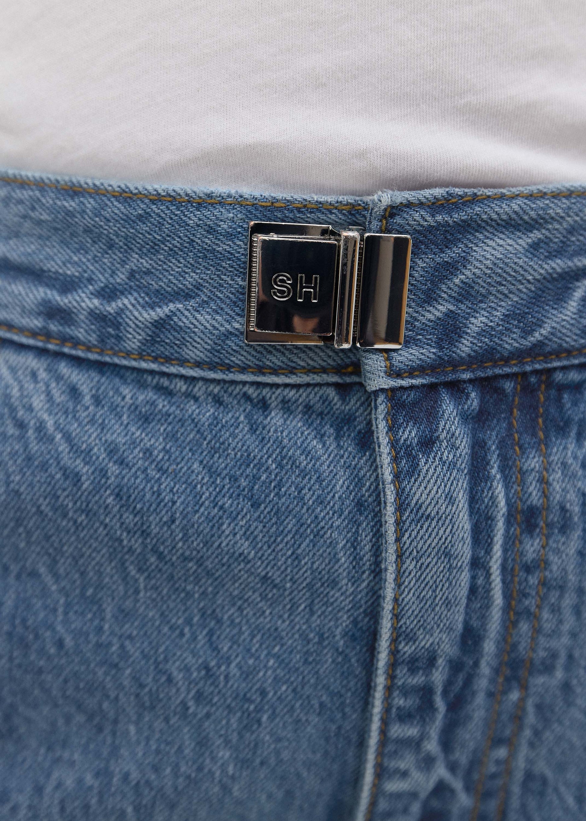 Close-up of a blue denim belt with a silver buckle featuring initials.