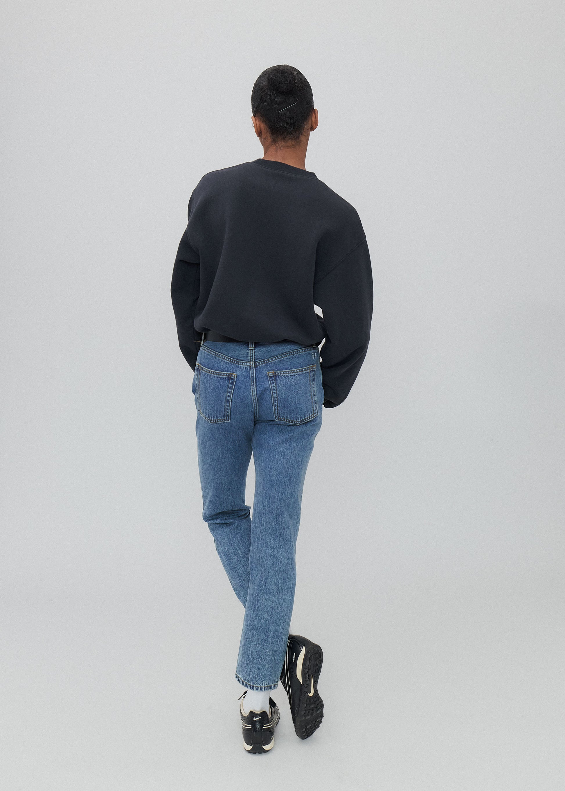 Person wearing a black sweater and blue jeans on a light gray background