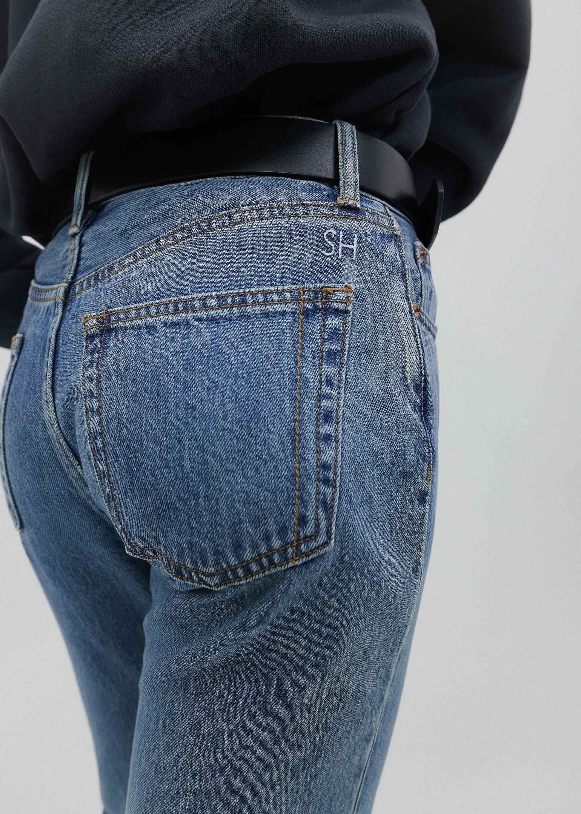 Person wearing blue jeans with a visible brand logo on a plain background