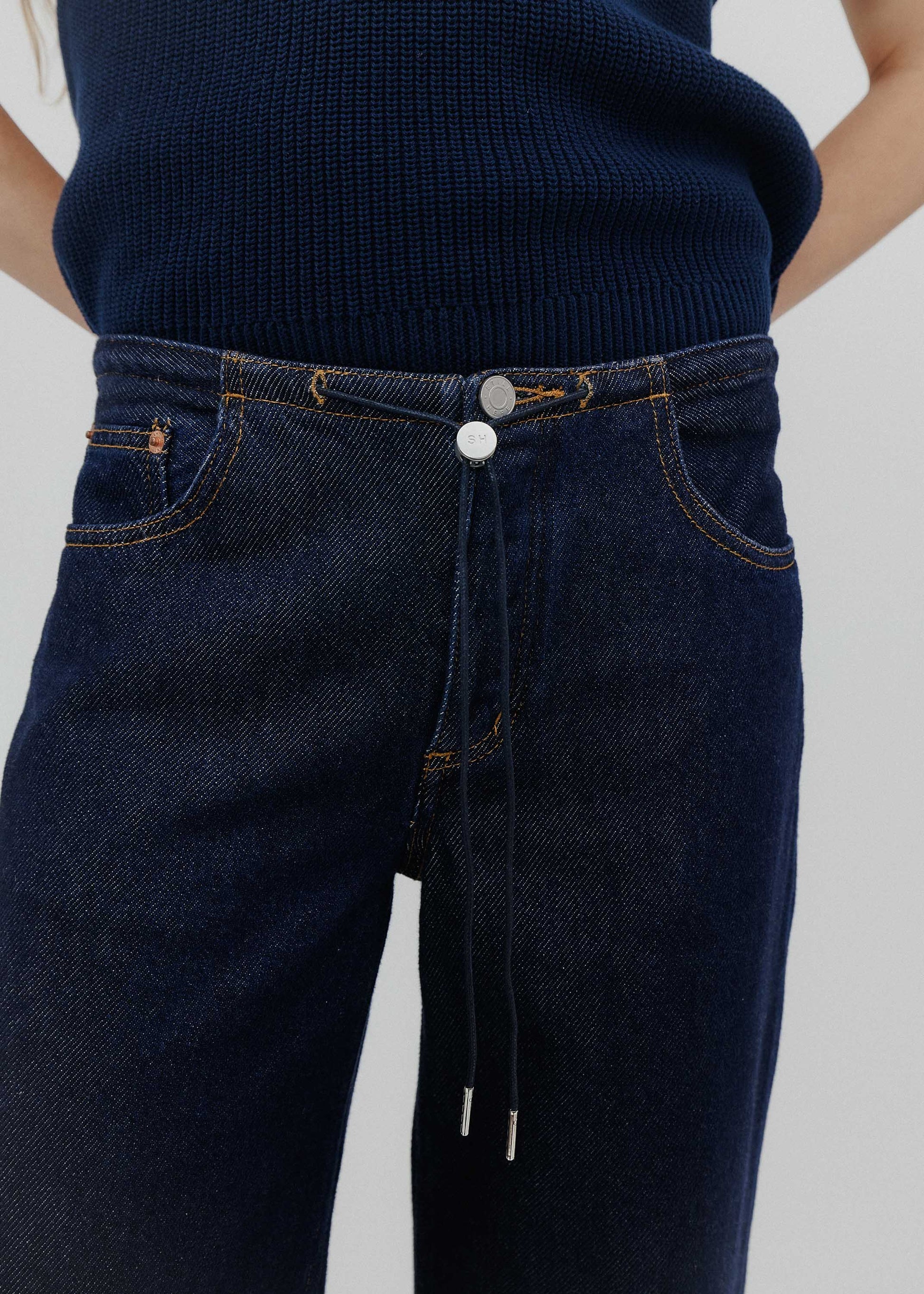 Dark blue jeans with a close-up of the waistband on a neutral background