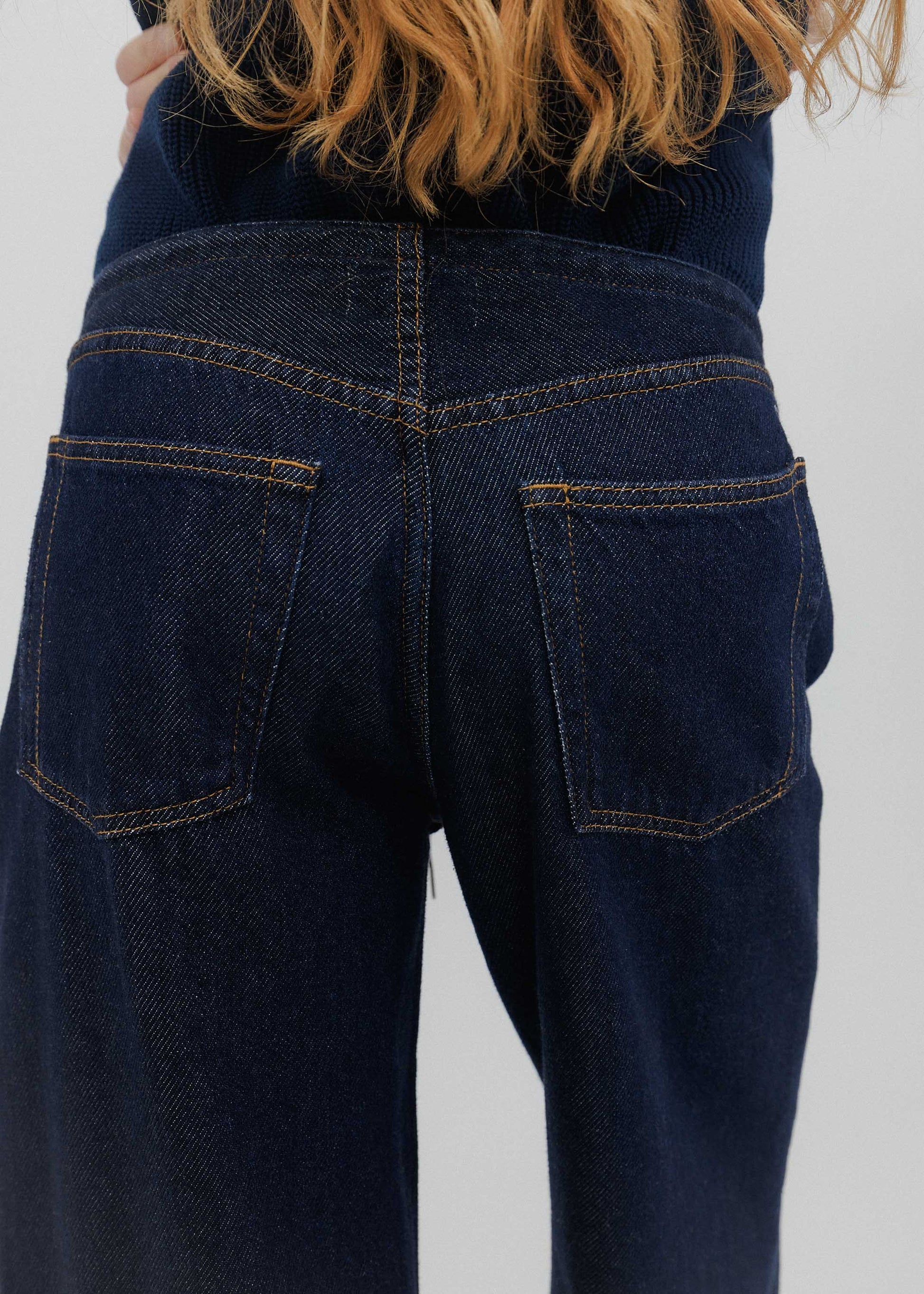 Dark blue jeans worn by a person on a plain background