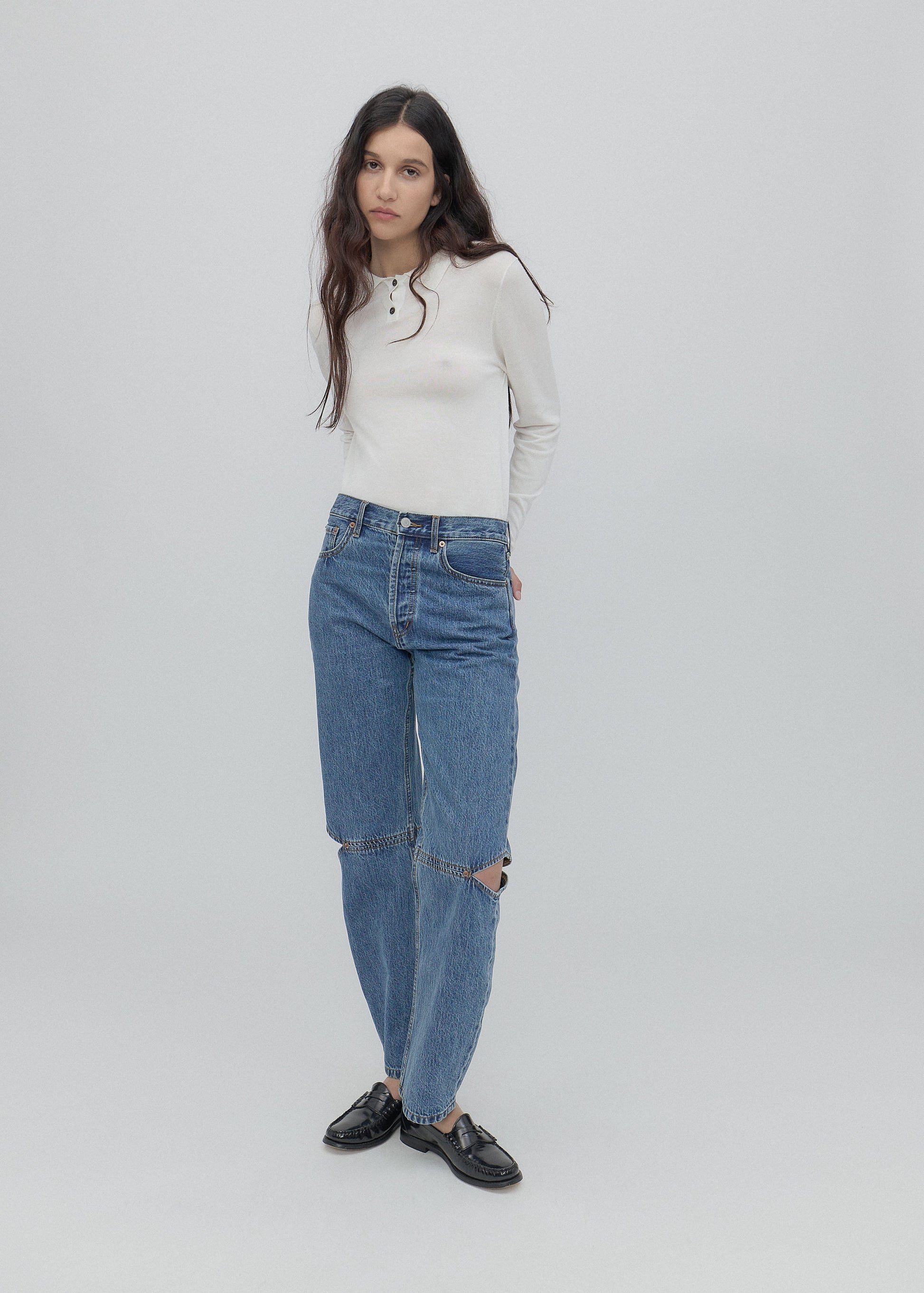 Woman wearing a white sweater and blue jeans on a light gray background