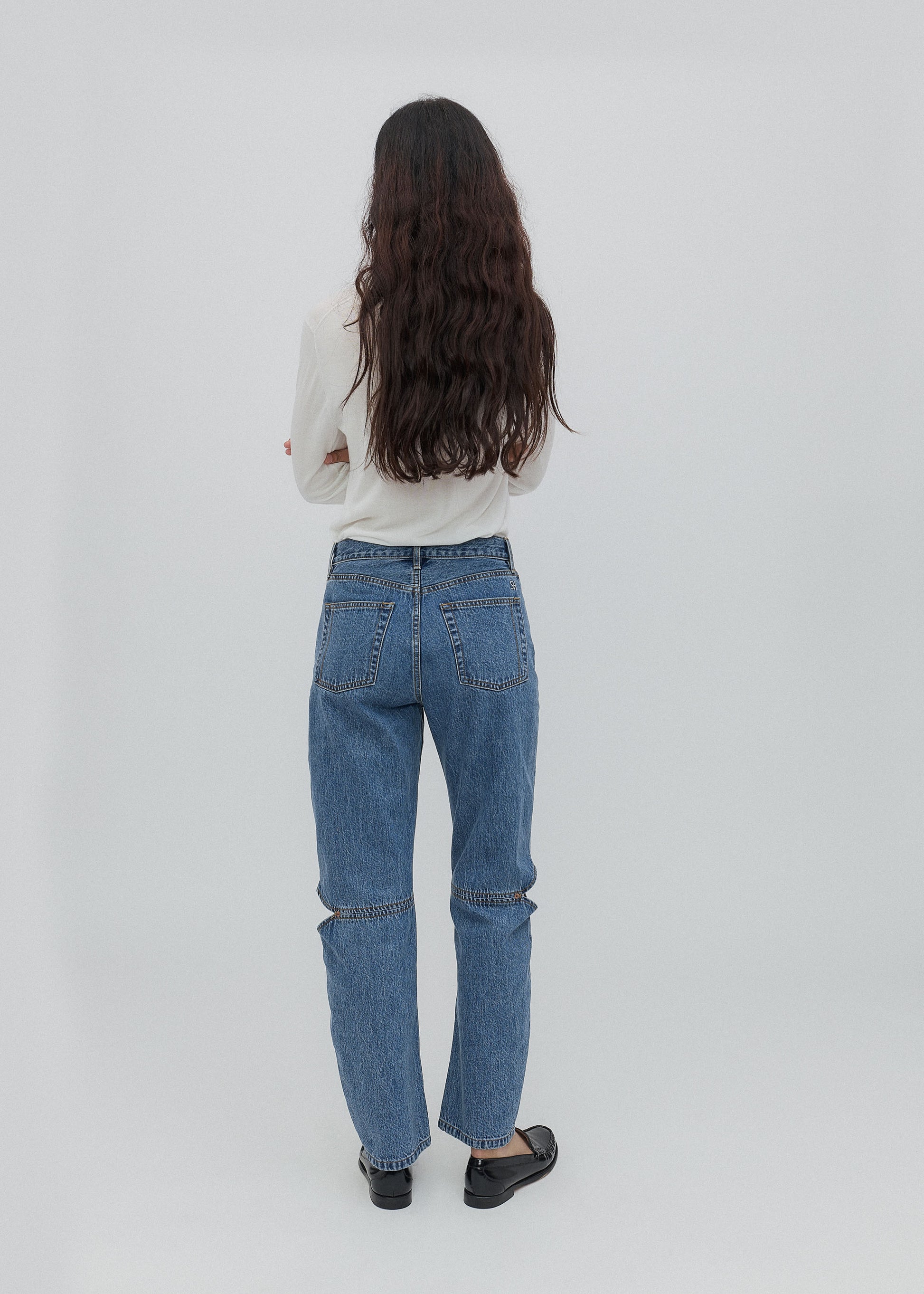 Person wearing blue jeans and a white top on a plain background
