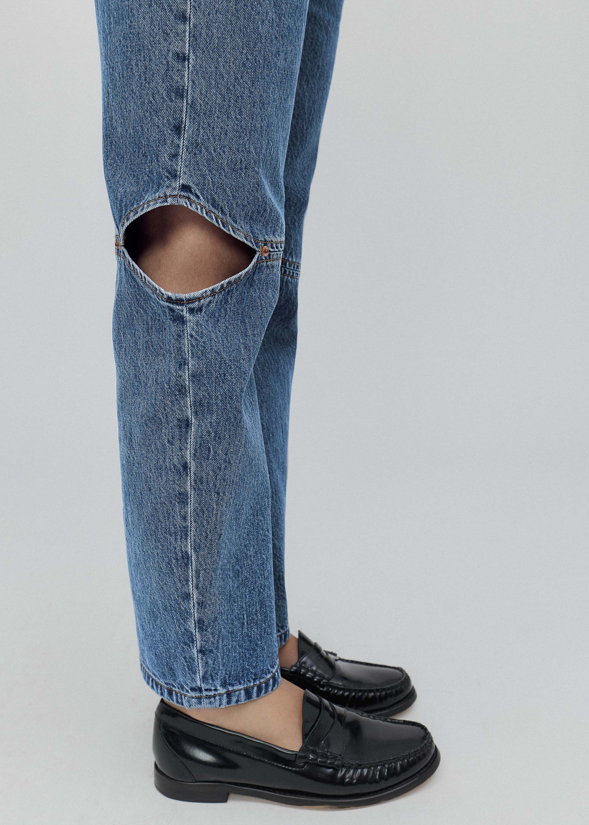 Ripped blue jeans worn with black shoes on a light gray background