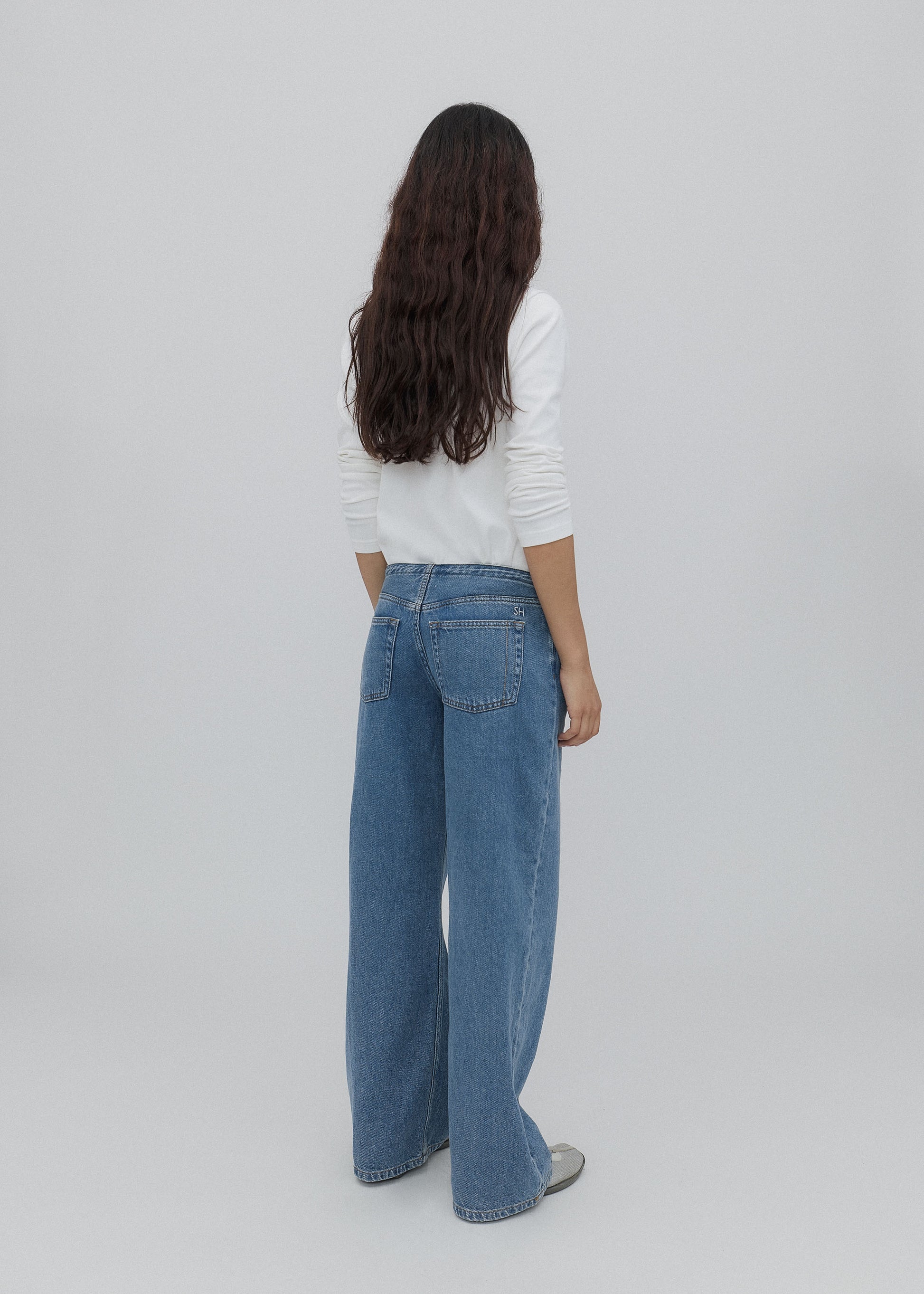 Person wearing a white sweater and blue jeans on a plain background