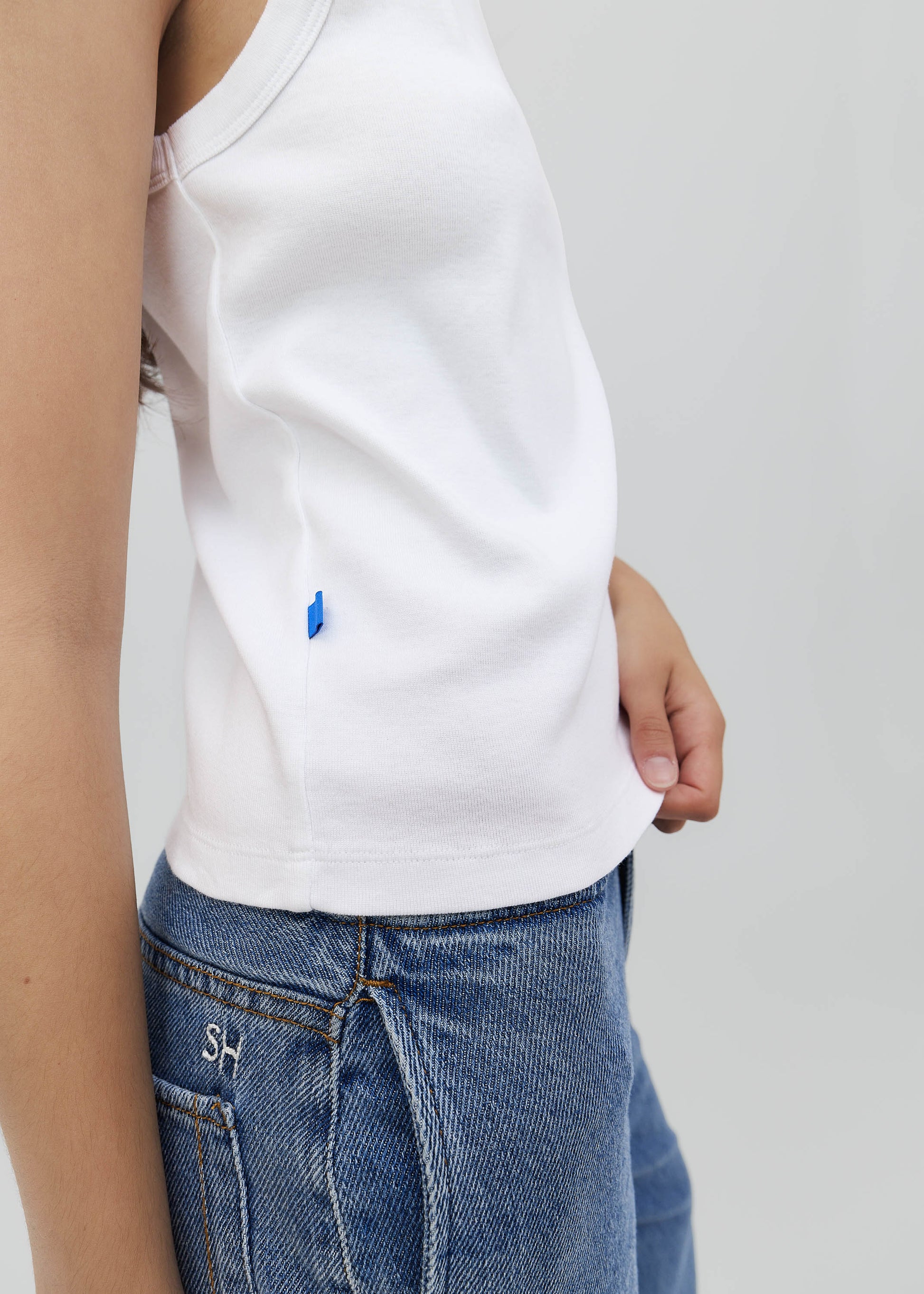 Person wearing a white t-shirt with a small blue logo and blue jeans on a plain background