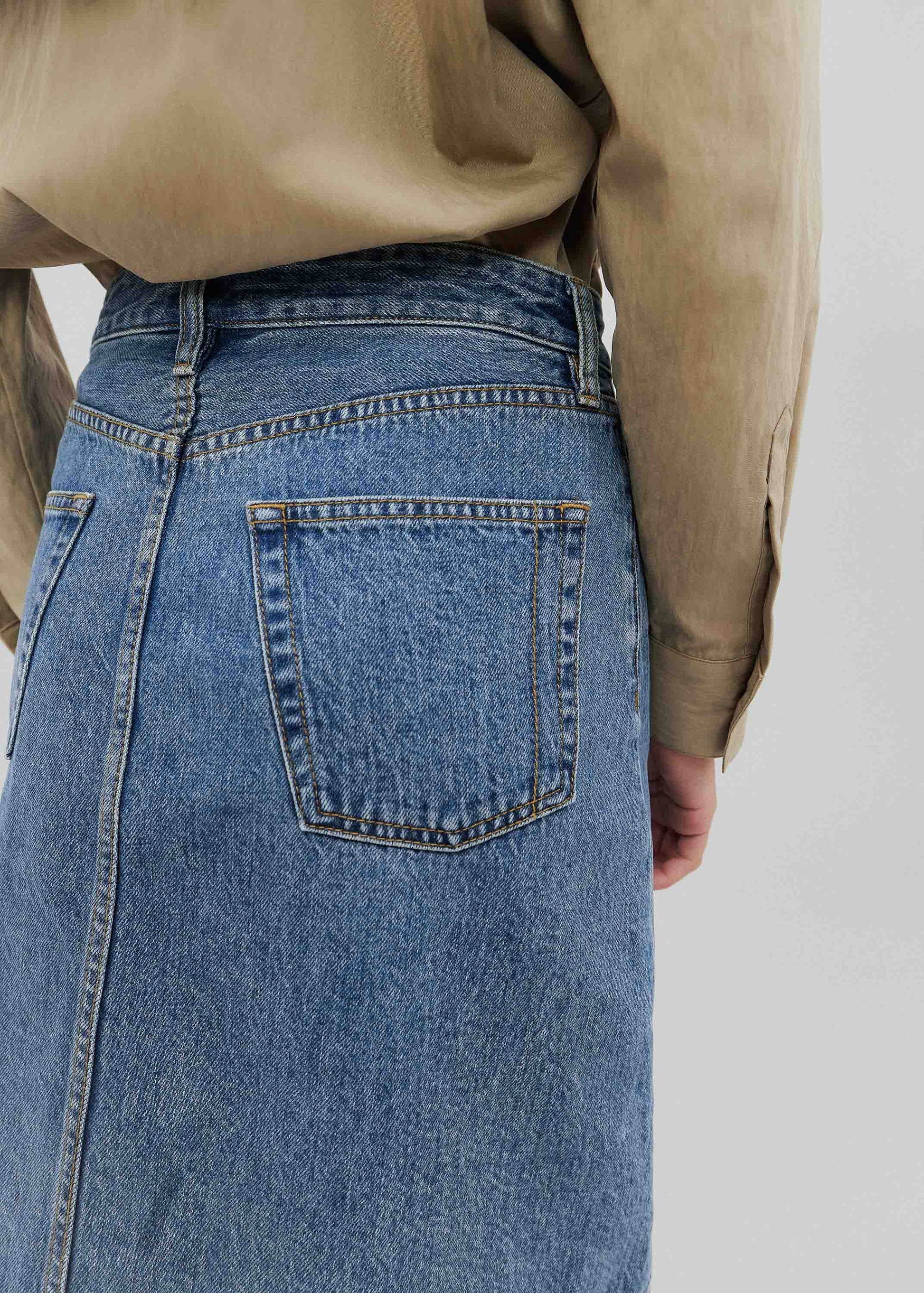 Person wearing a beige shirt and blue denim skirt on a plain background