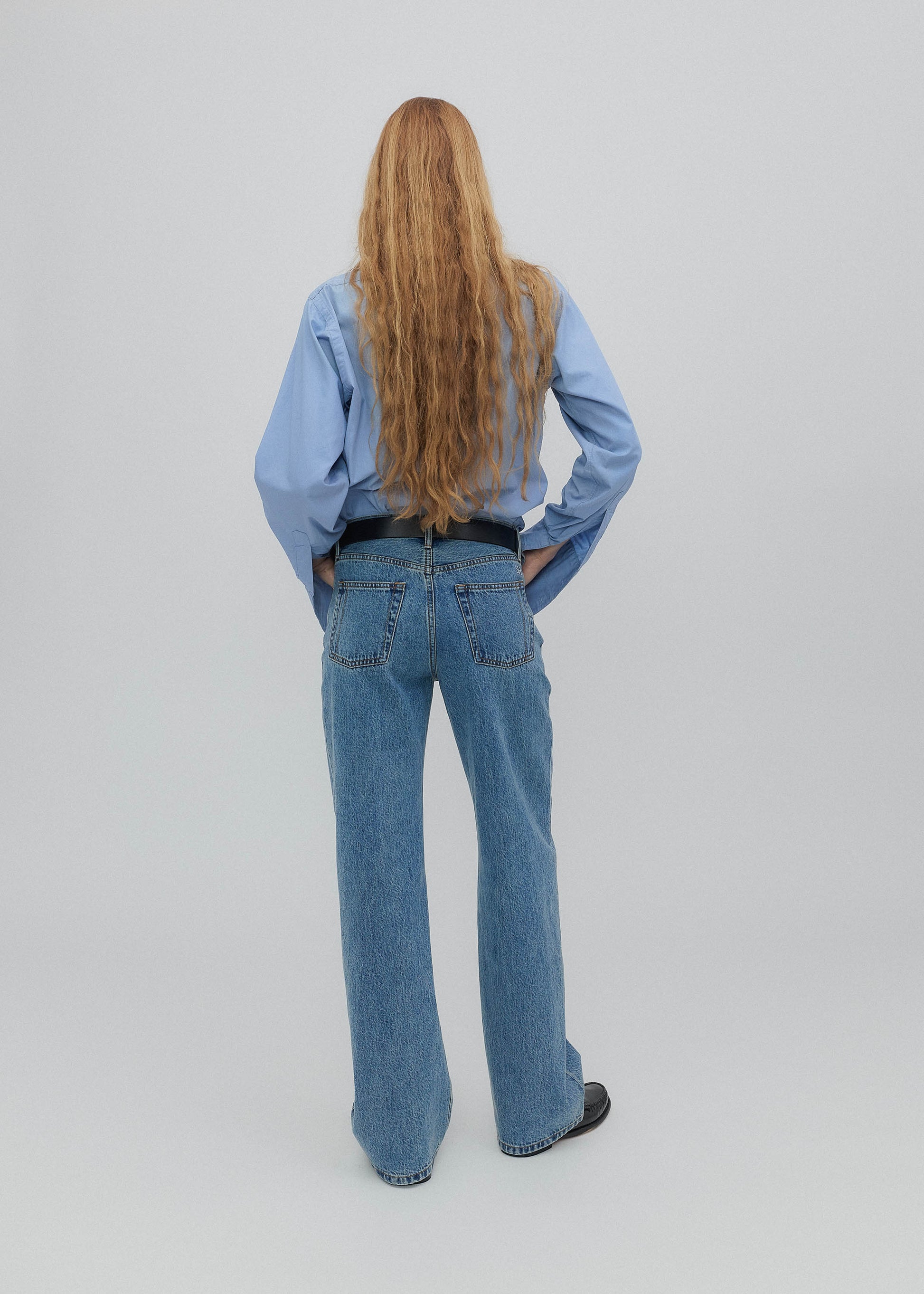 Person wearing blue jeans and a light blue shirt on a plain background