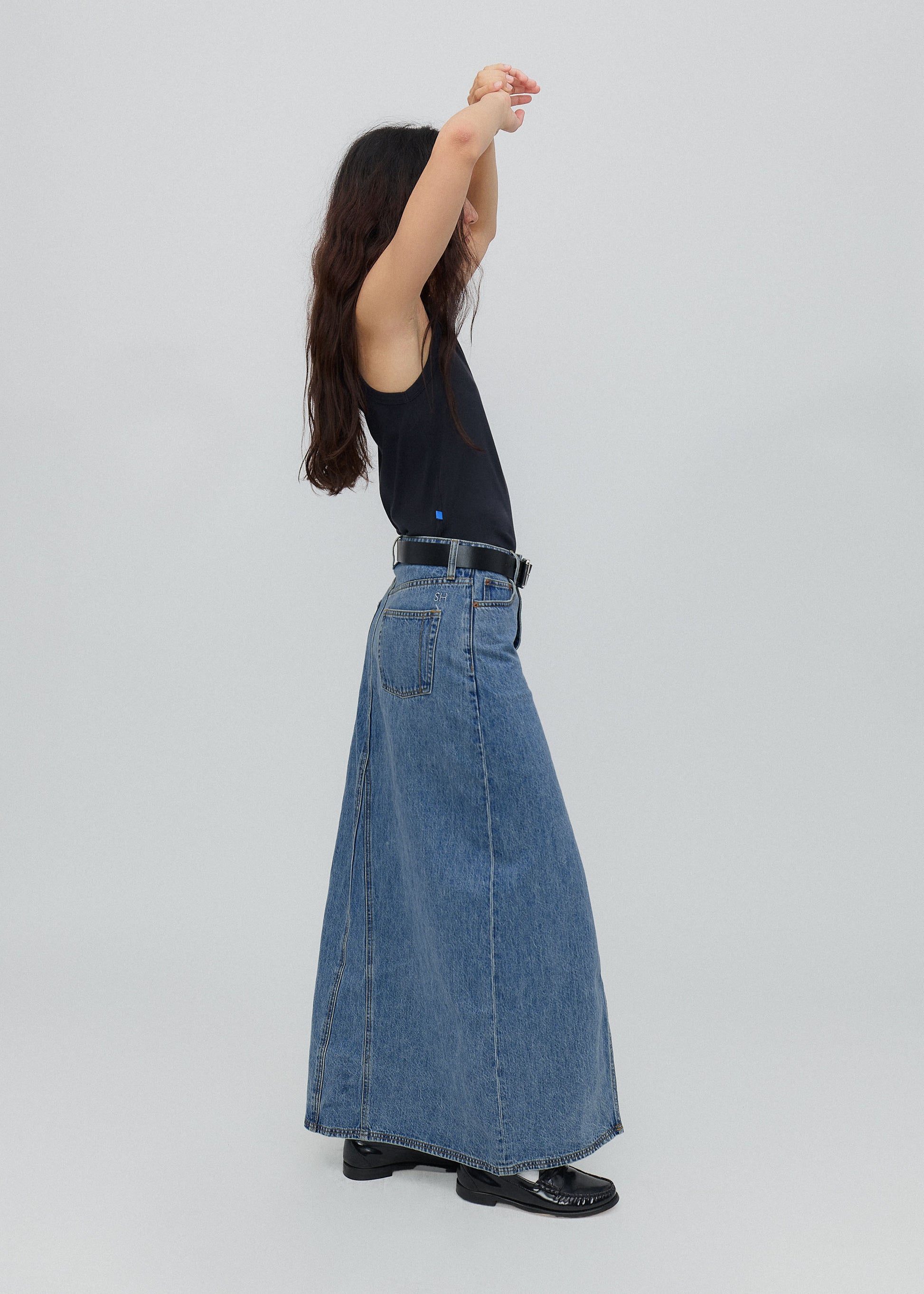 Person wearing a long blue denim skirt on a plain background