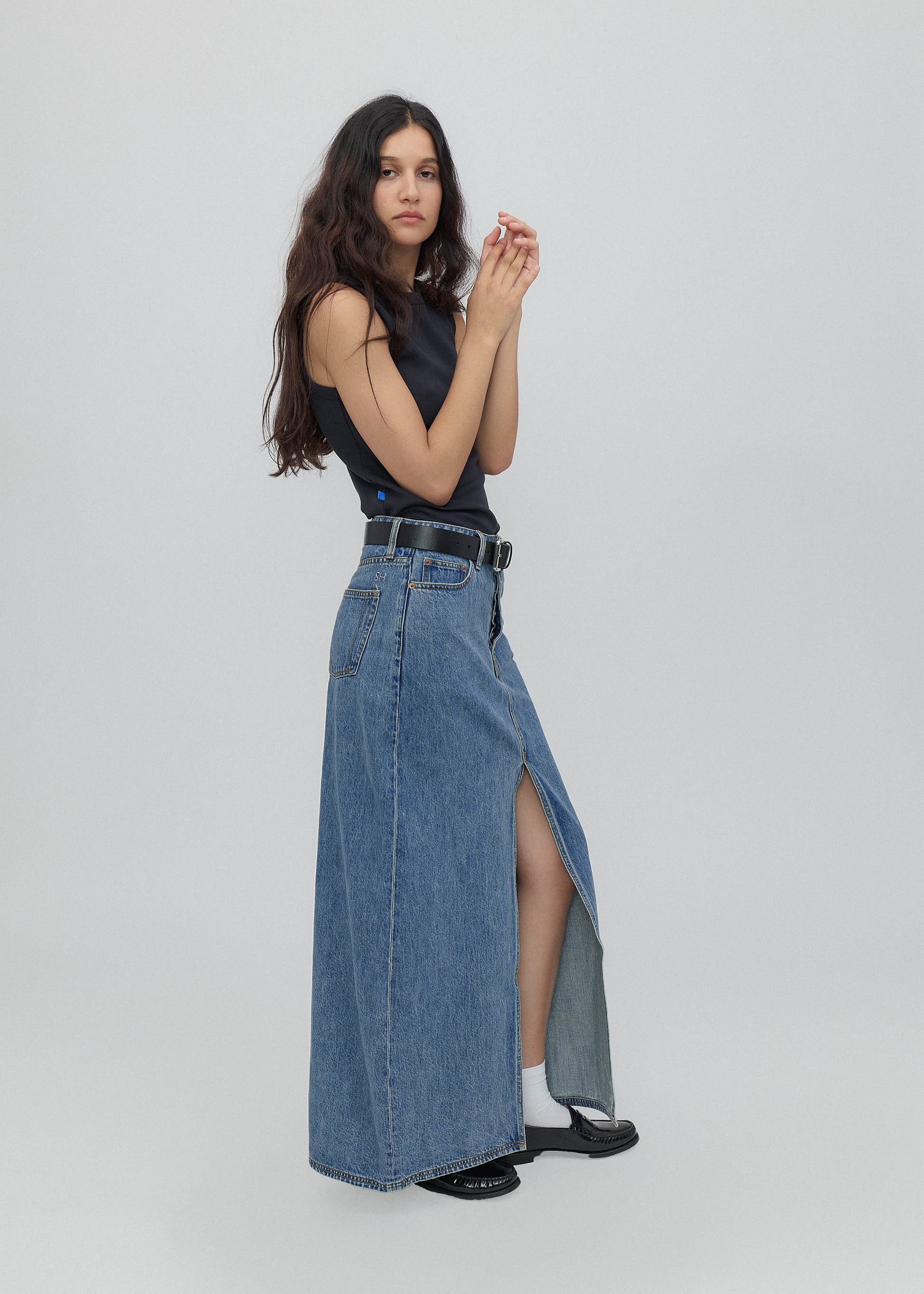 Woman wearing a long denim skirt with a high slit on a white background