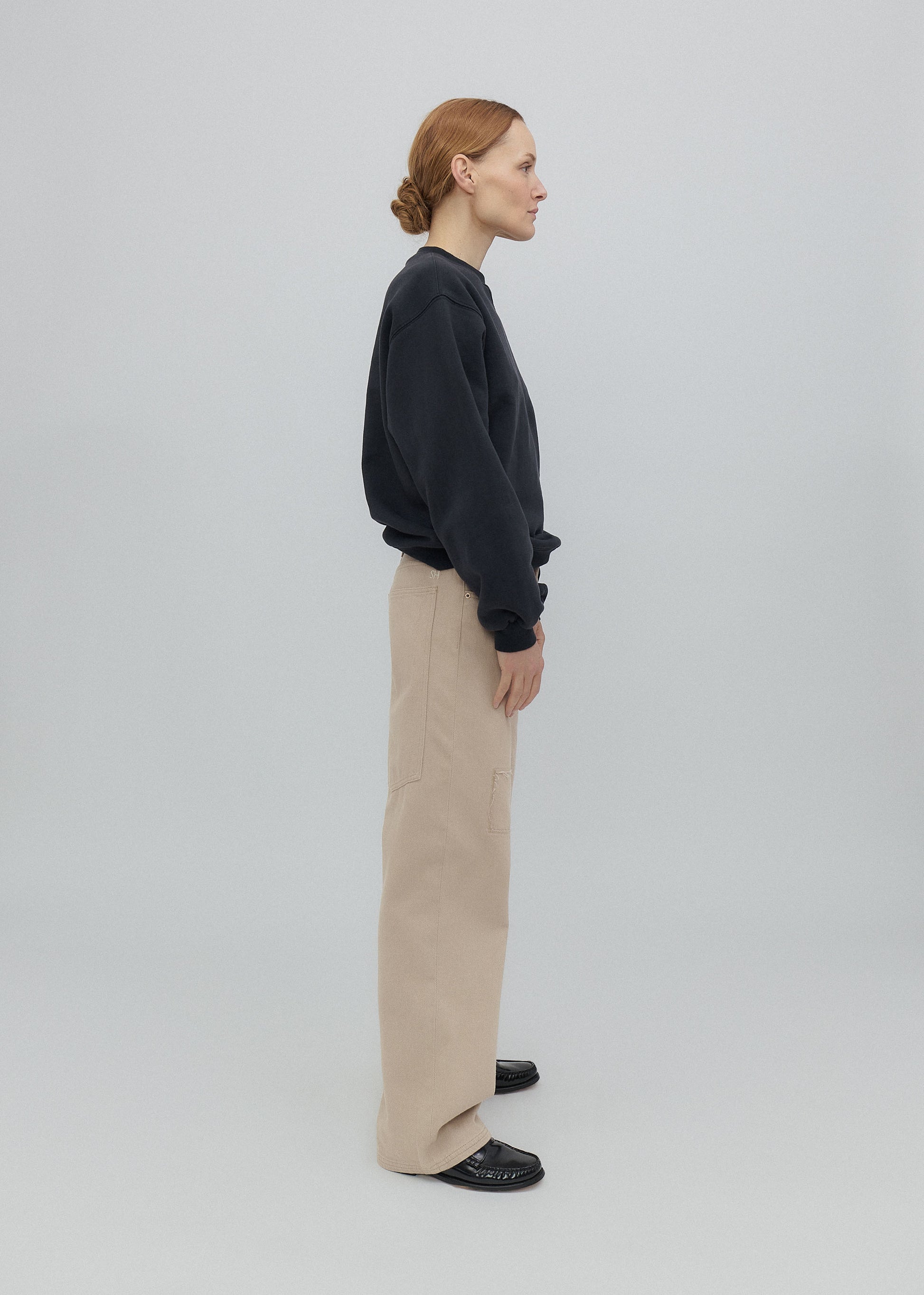 Person wearing a dark sweater and beige pants on a light gray background