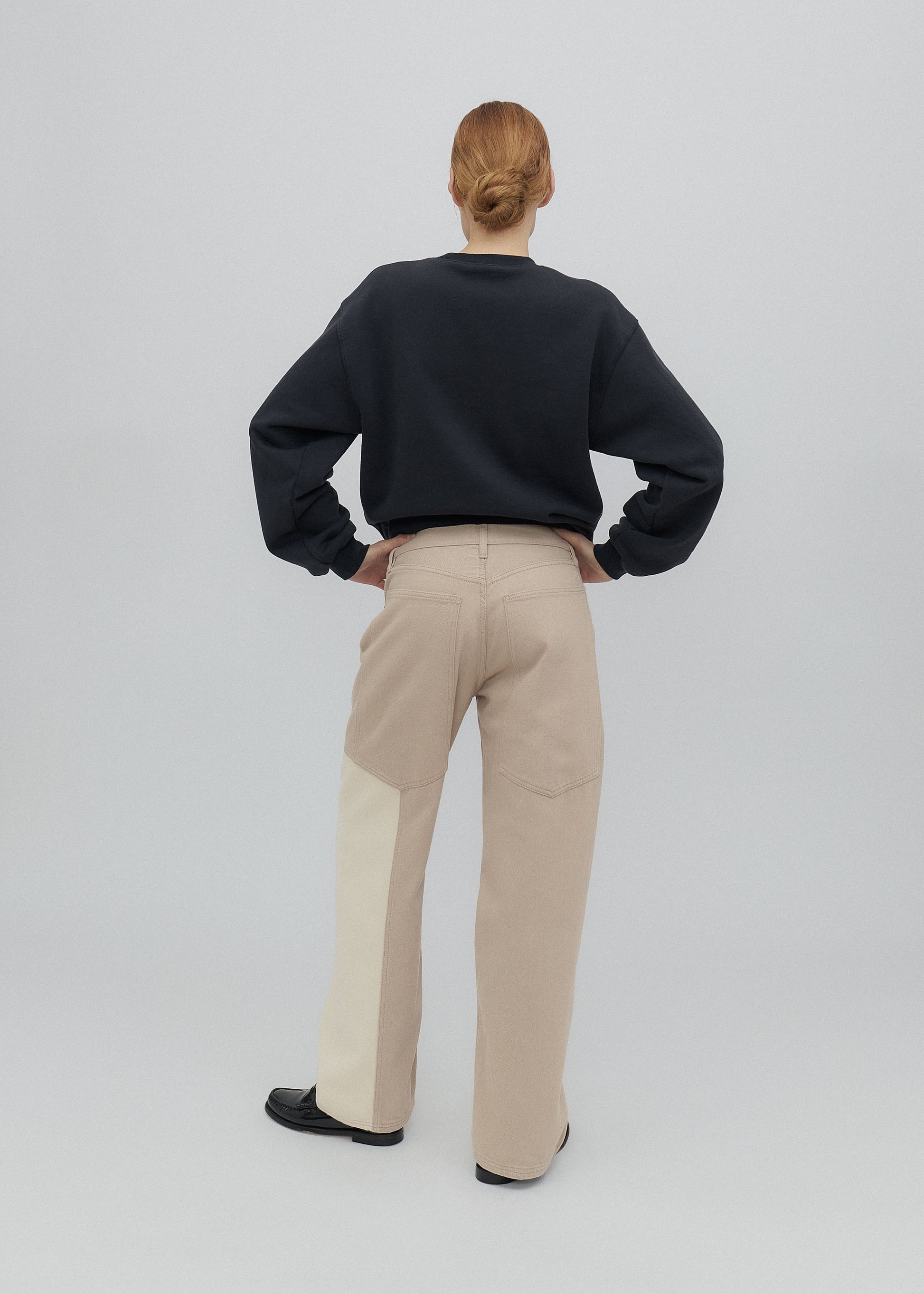 Person wearing a black sweater and beige pants on a white background
