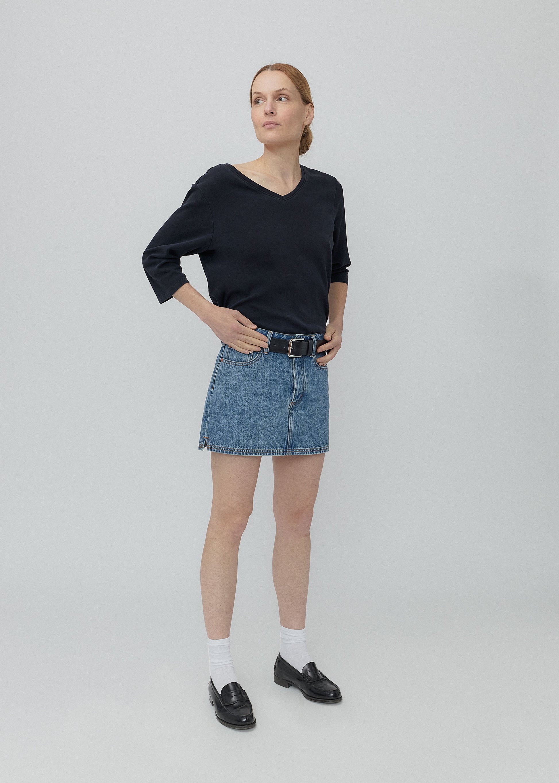 Woman wearing a black sweater and denim skirt on a plain background