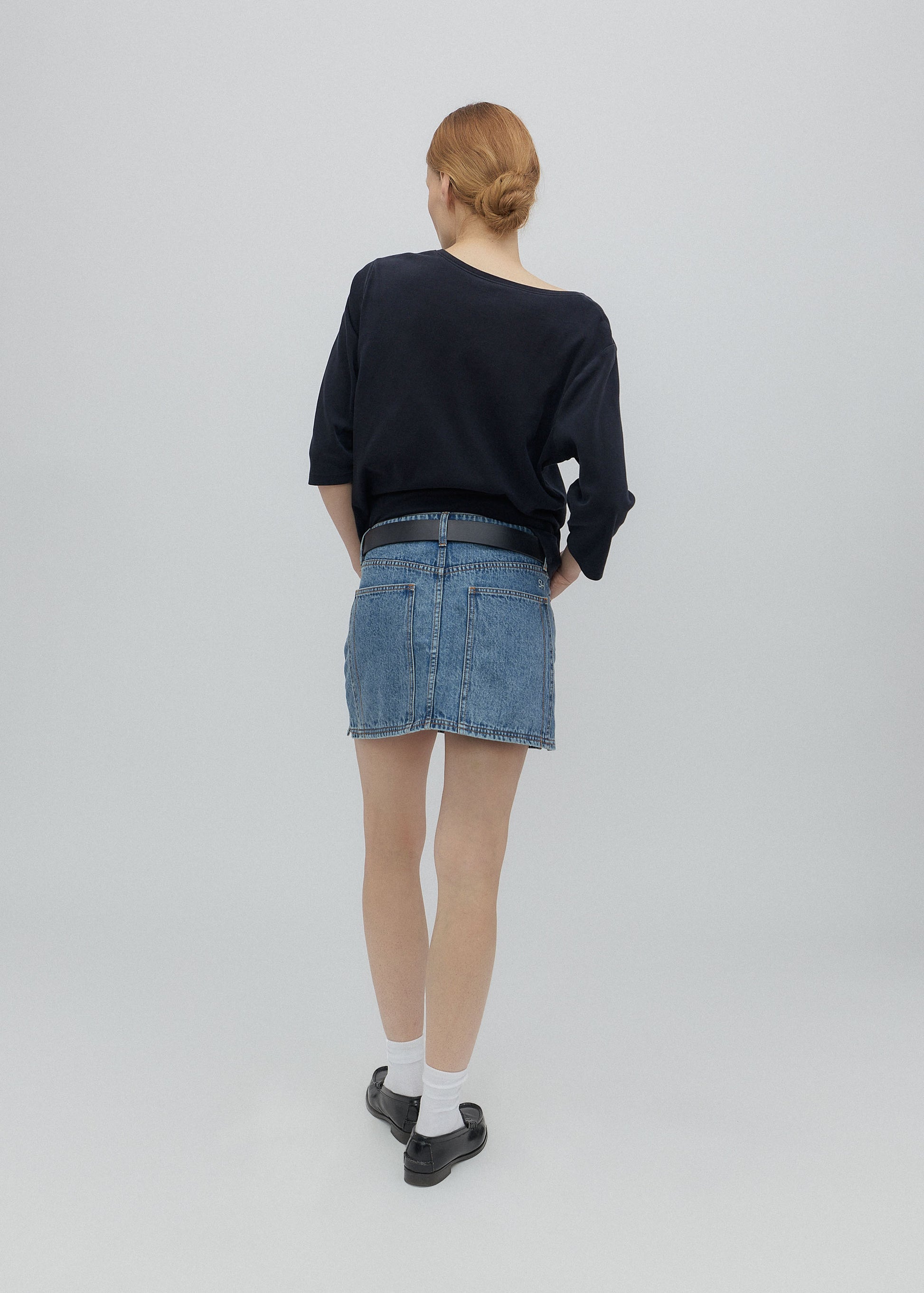 Person wearing a black sweater and blue denim skirt on a plain background