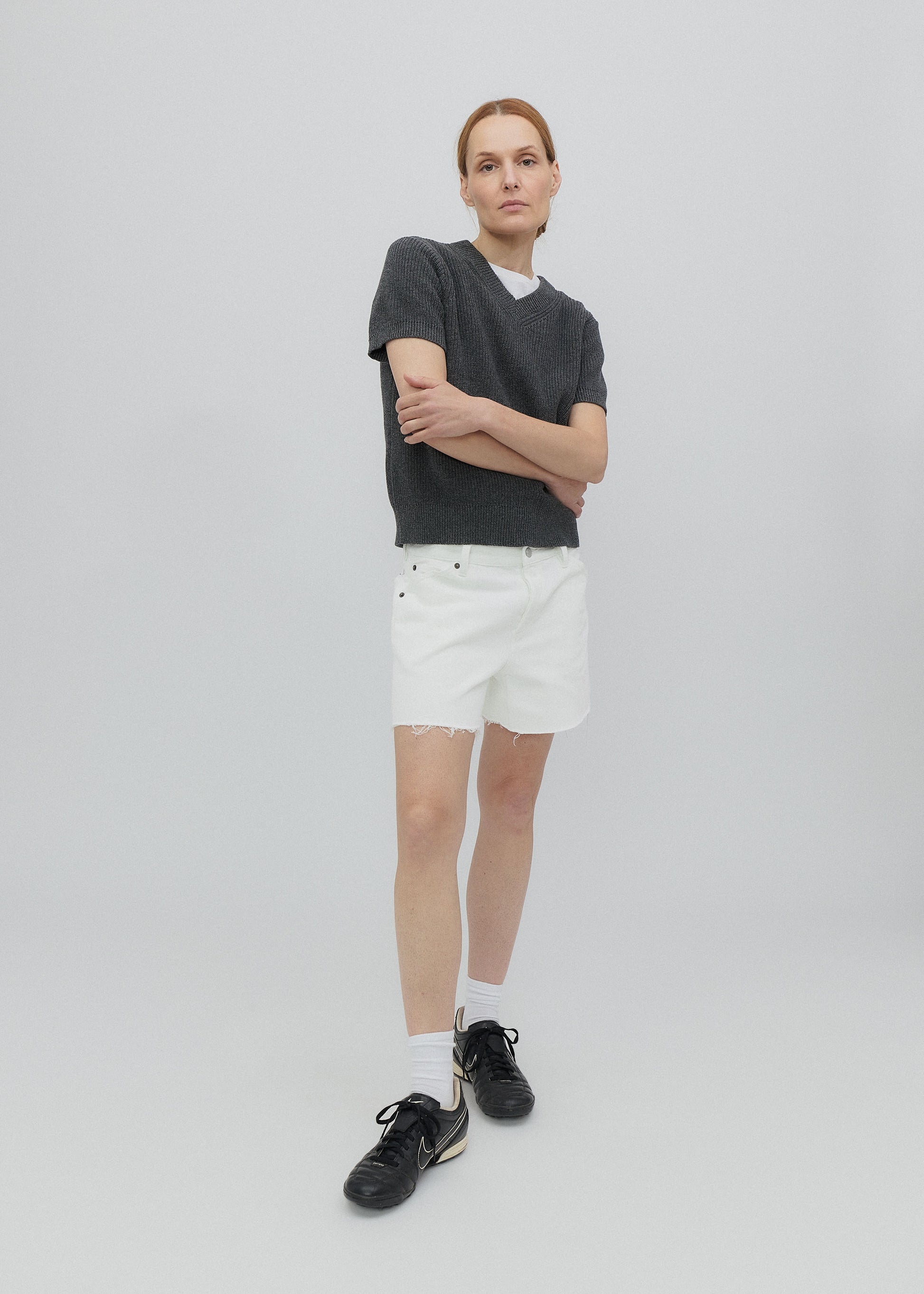 Person wearing a dark gray t-shirt, white shorts, and black shoes on a light gray background