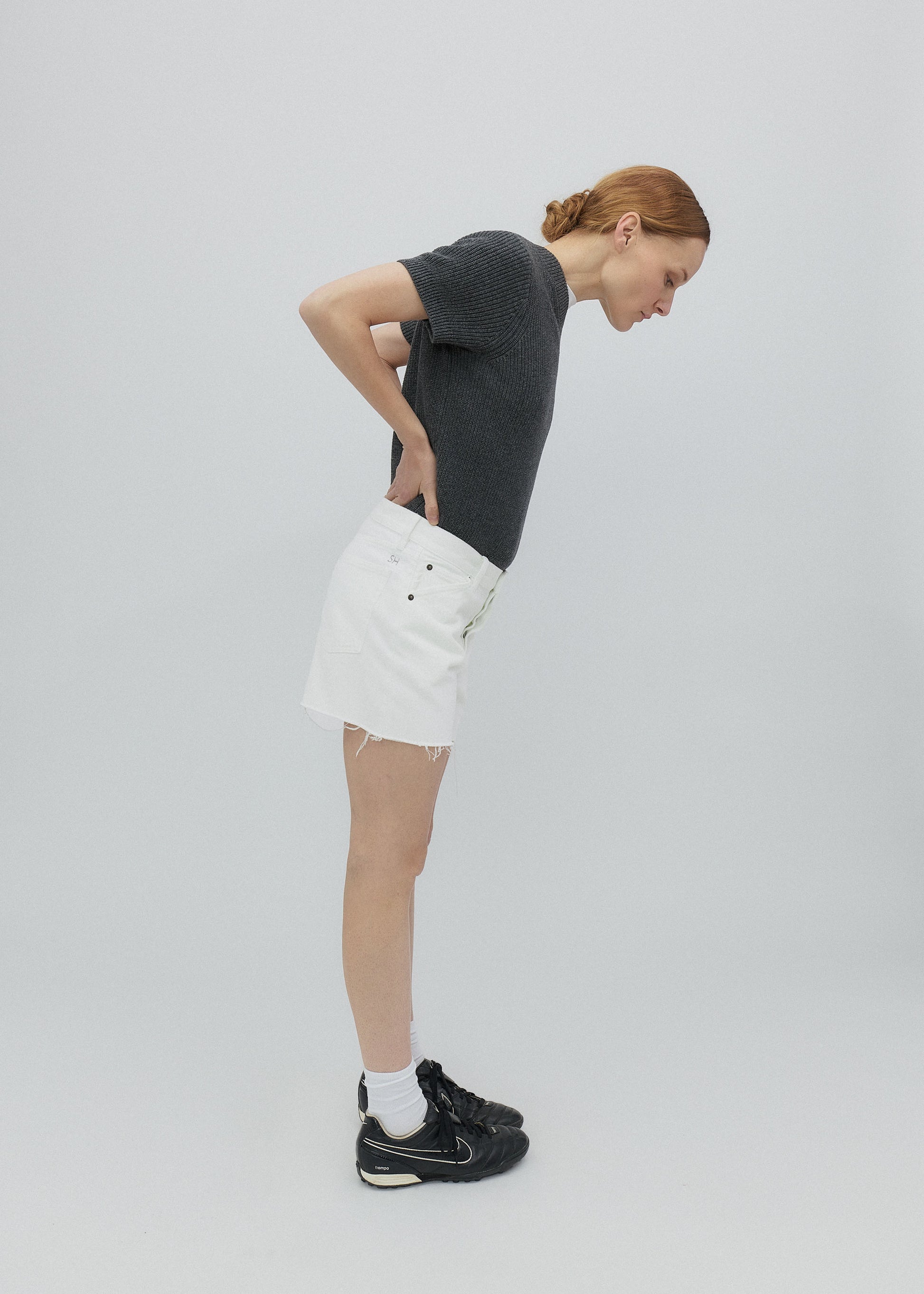 Person wearing a dark t-shirt, white shorts, and black shoes on a light gray background