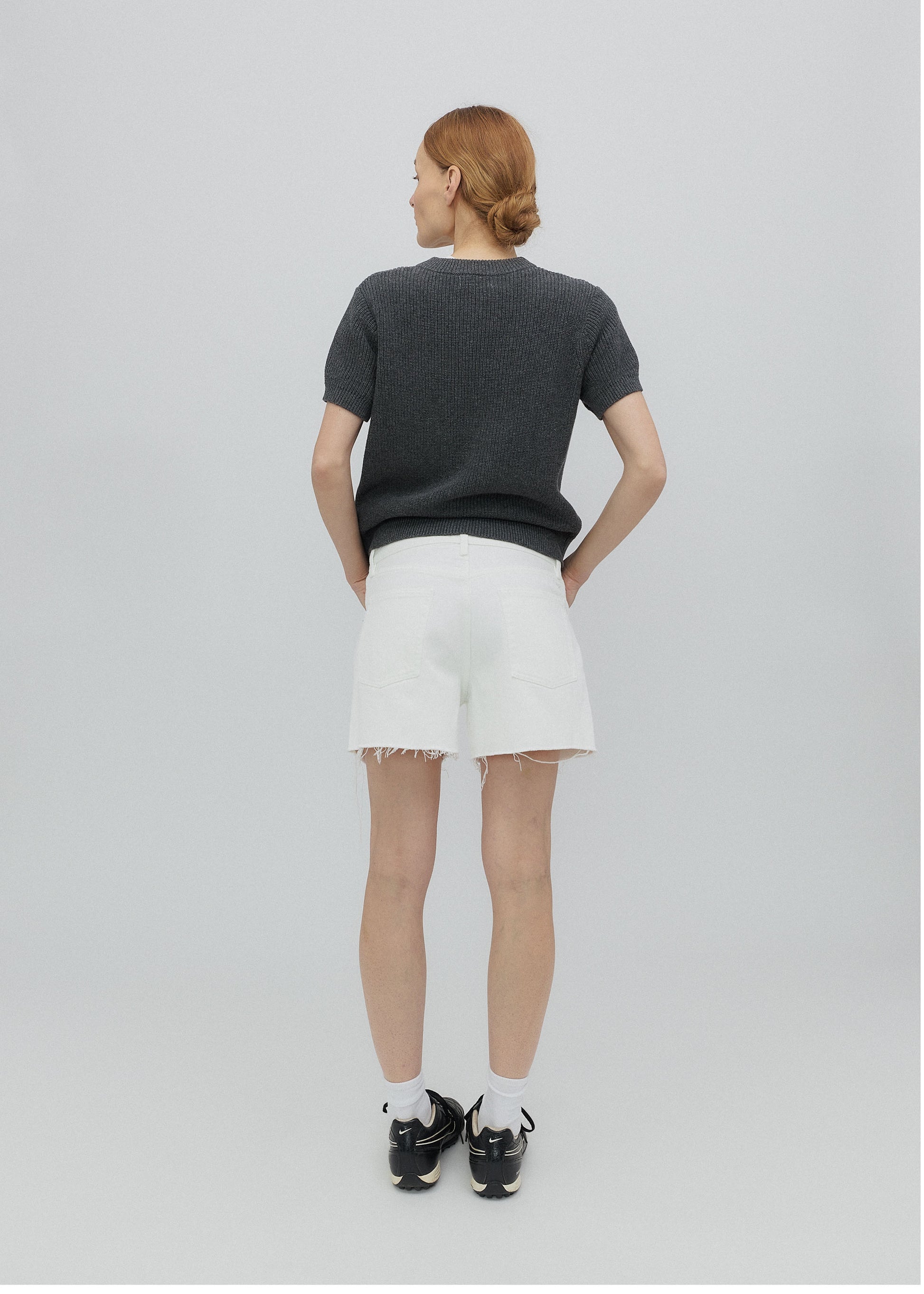 Person wearing a dark gray t-shirt and white shorts on a light gray background