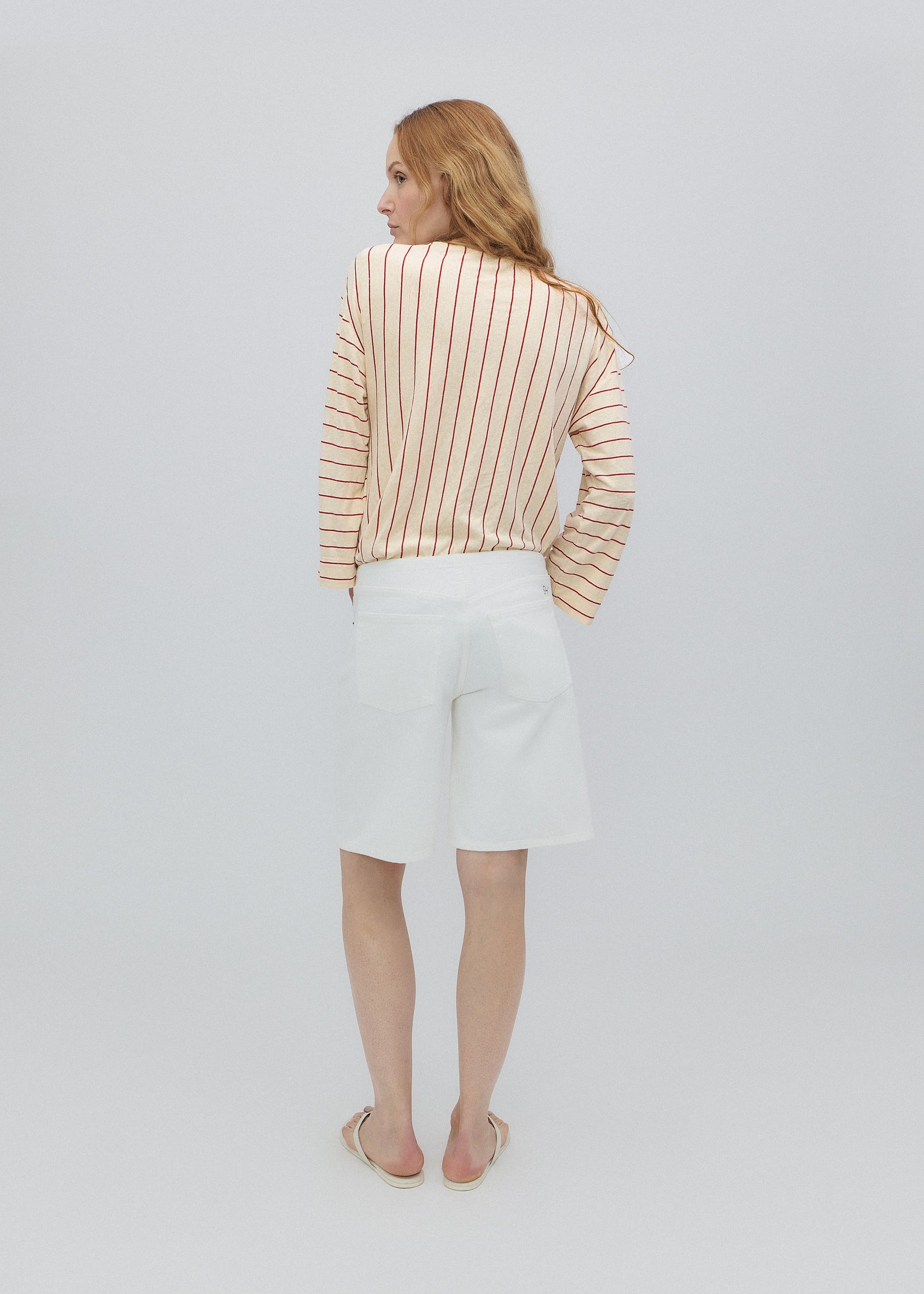 Woman wearing a striped shirt and white pants on a plain background