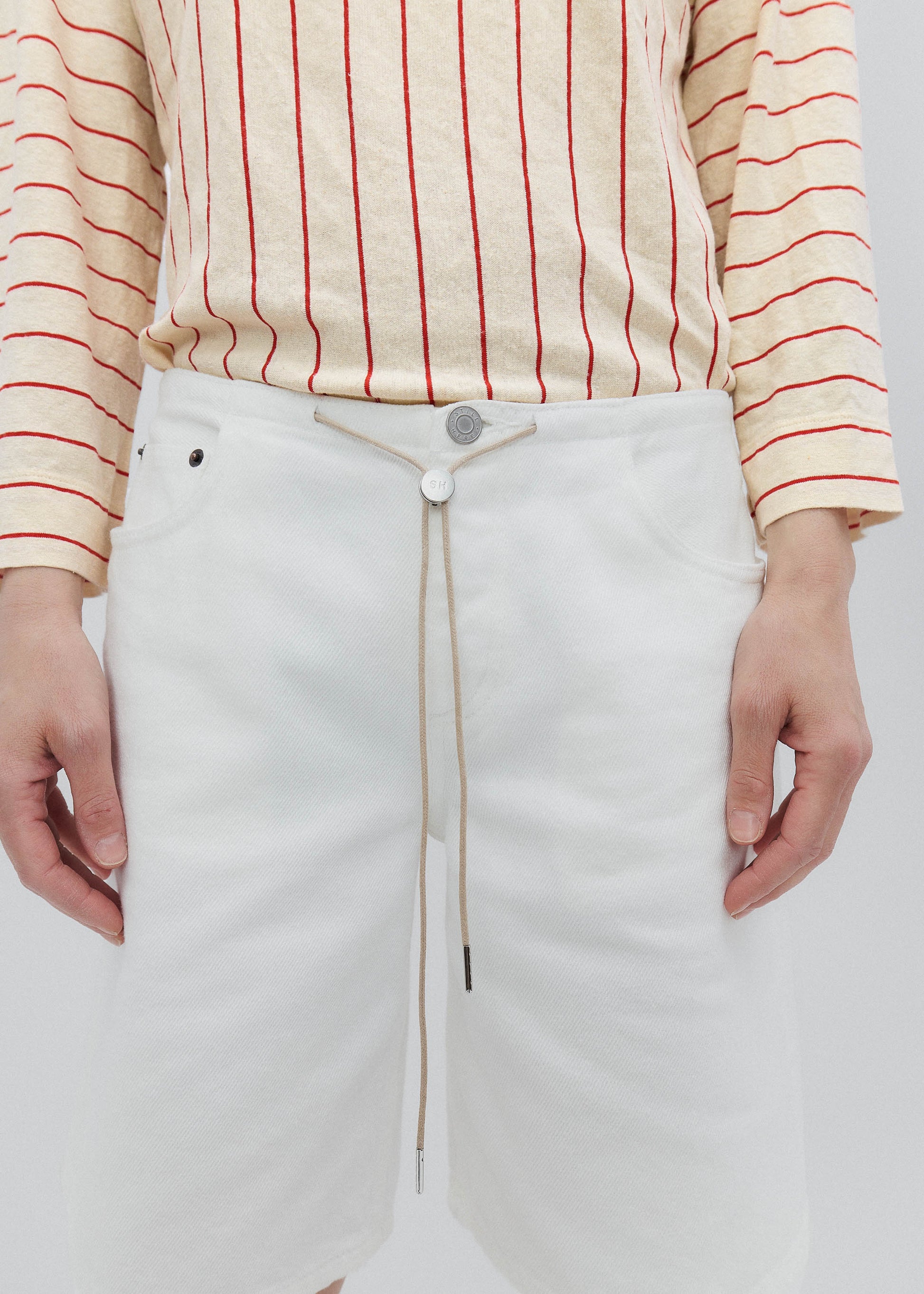 Person wearing a cream-colored top with red stripes and white pants on a plain background