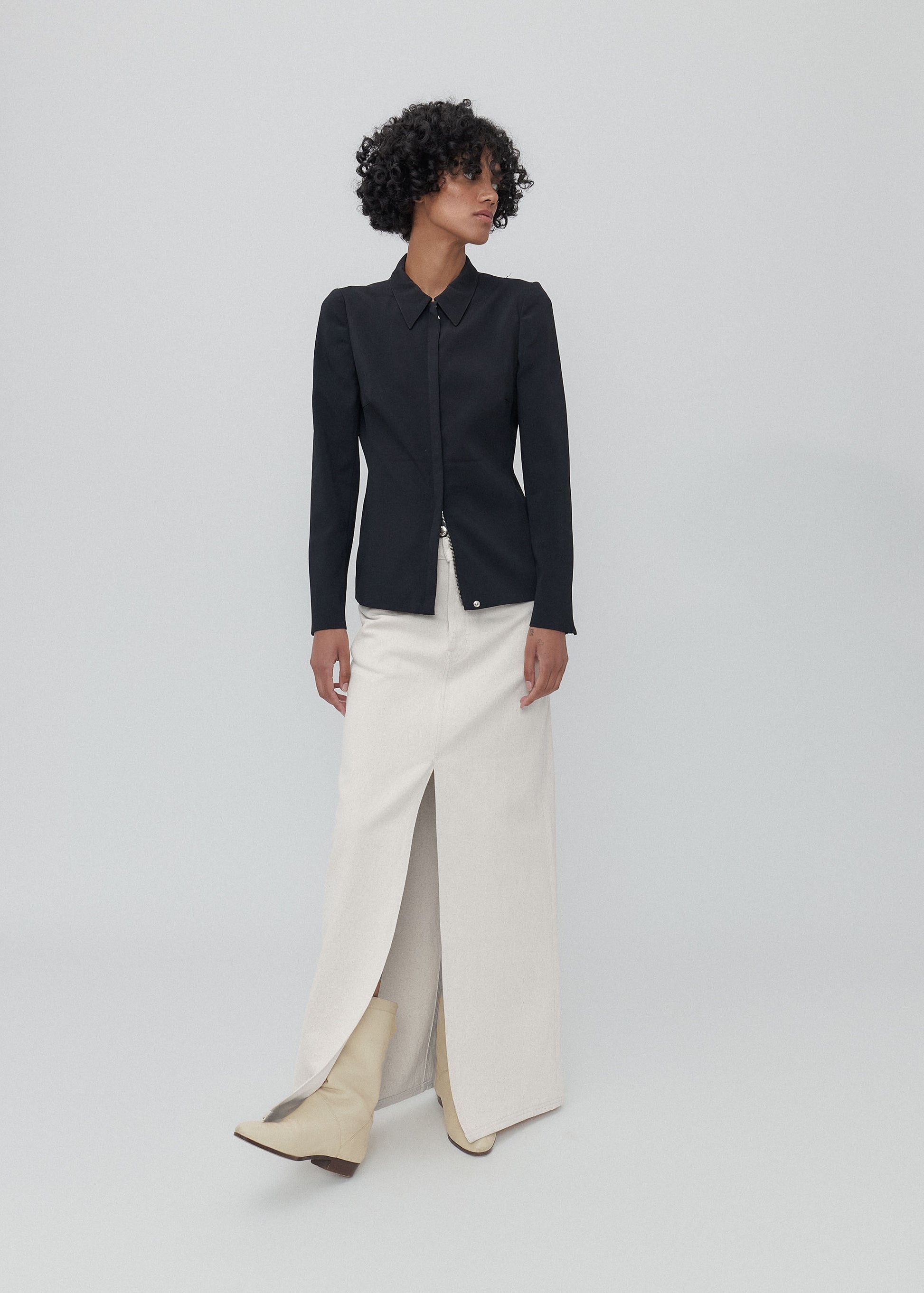 Person wearing a black jacket and white pants on a light gray background