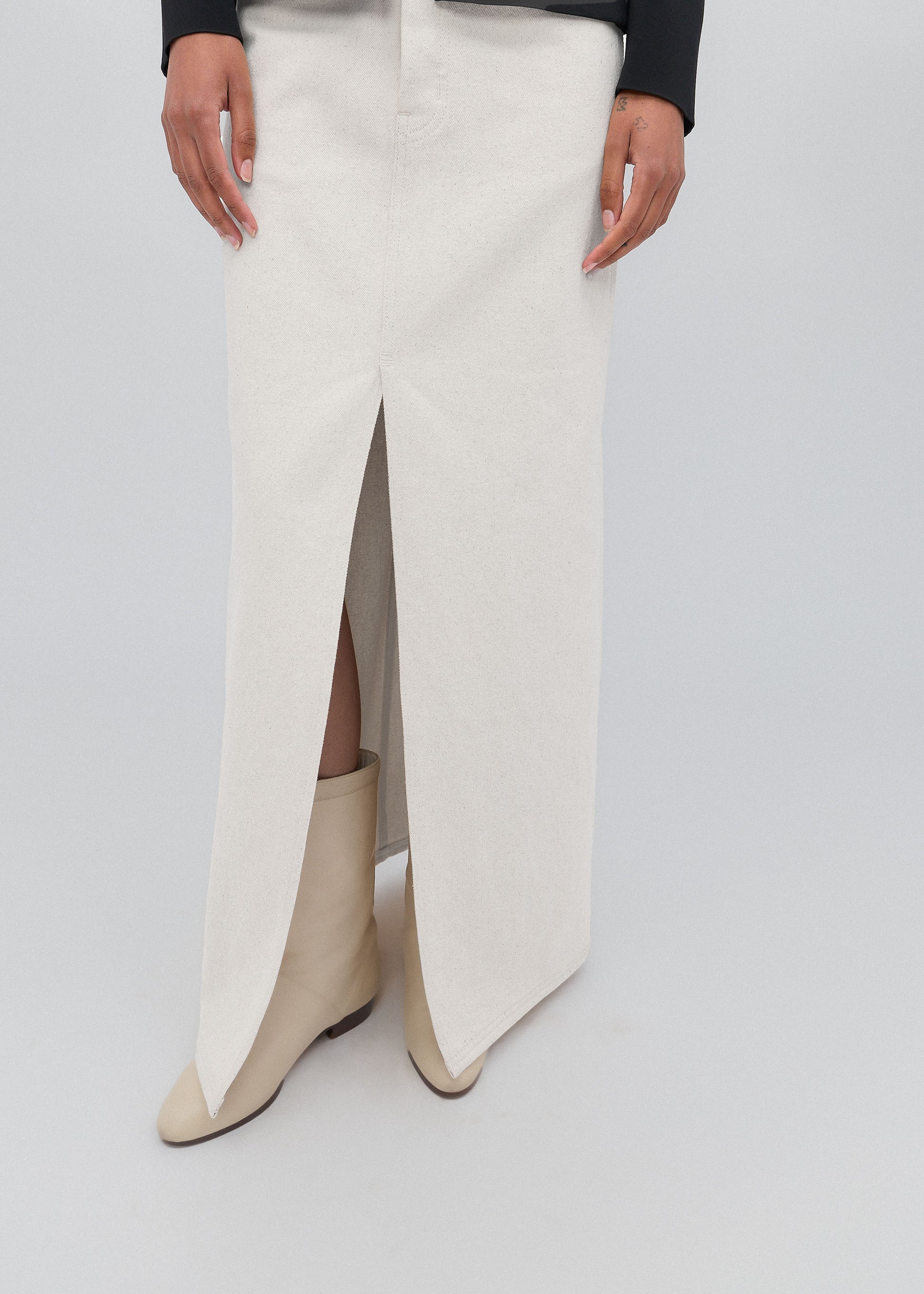 White skirt with a high slit and beige boots on a light gray background