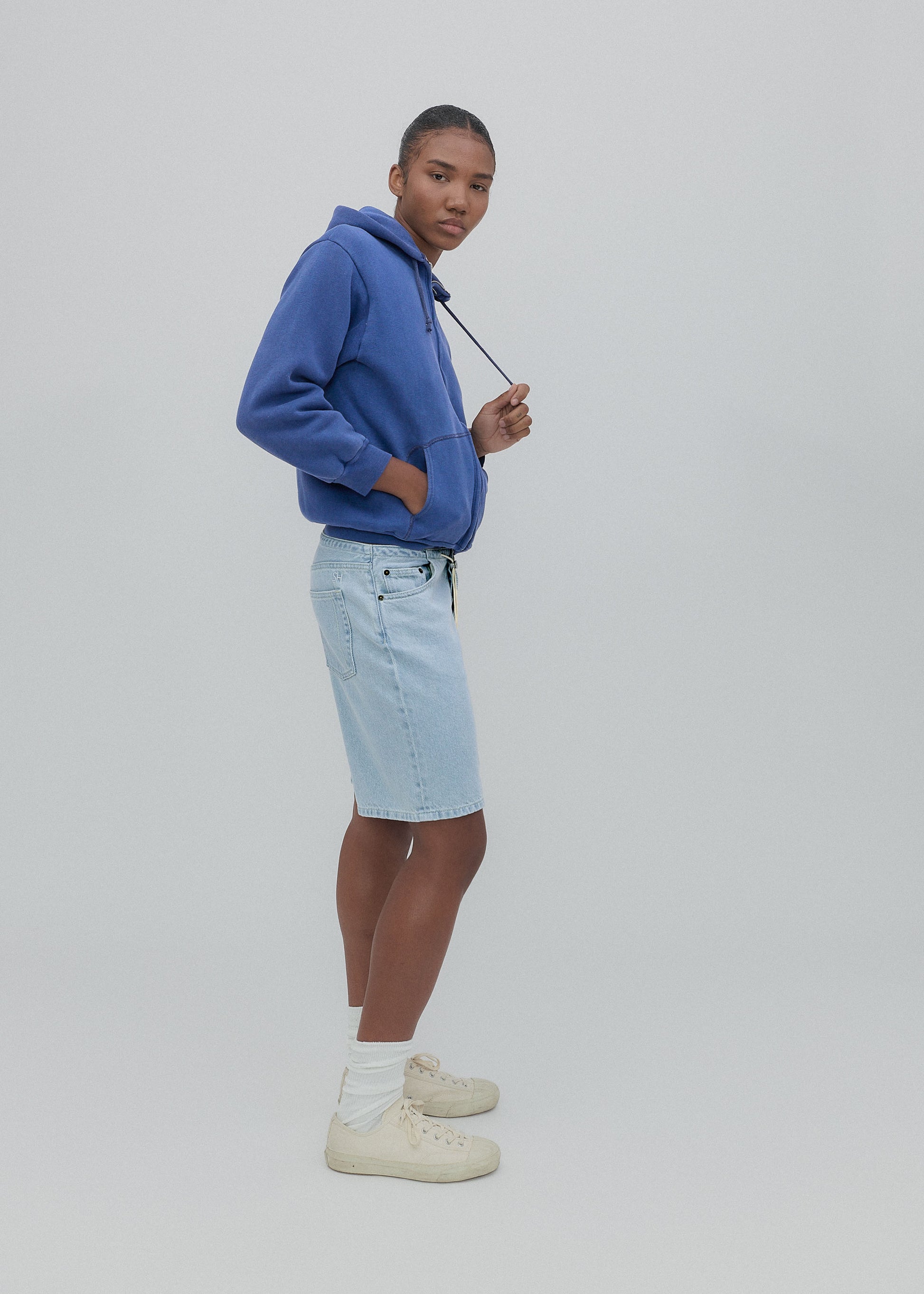 Person wearing a blue hoodie and light blue shorts on a plain background