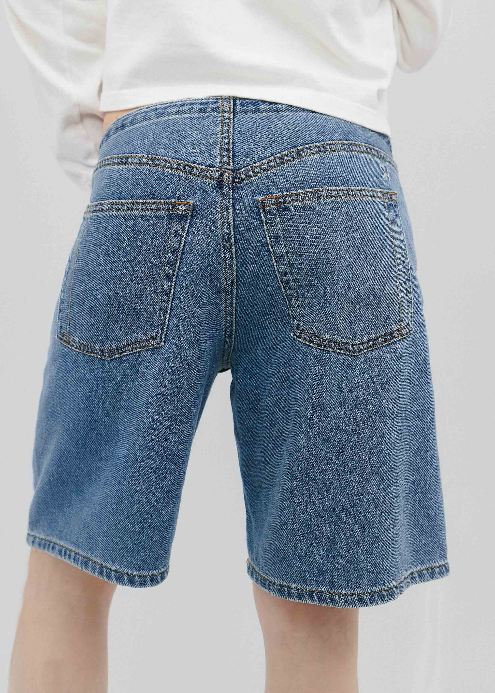 Blue denim shorts worn by a person on a plain background