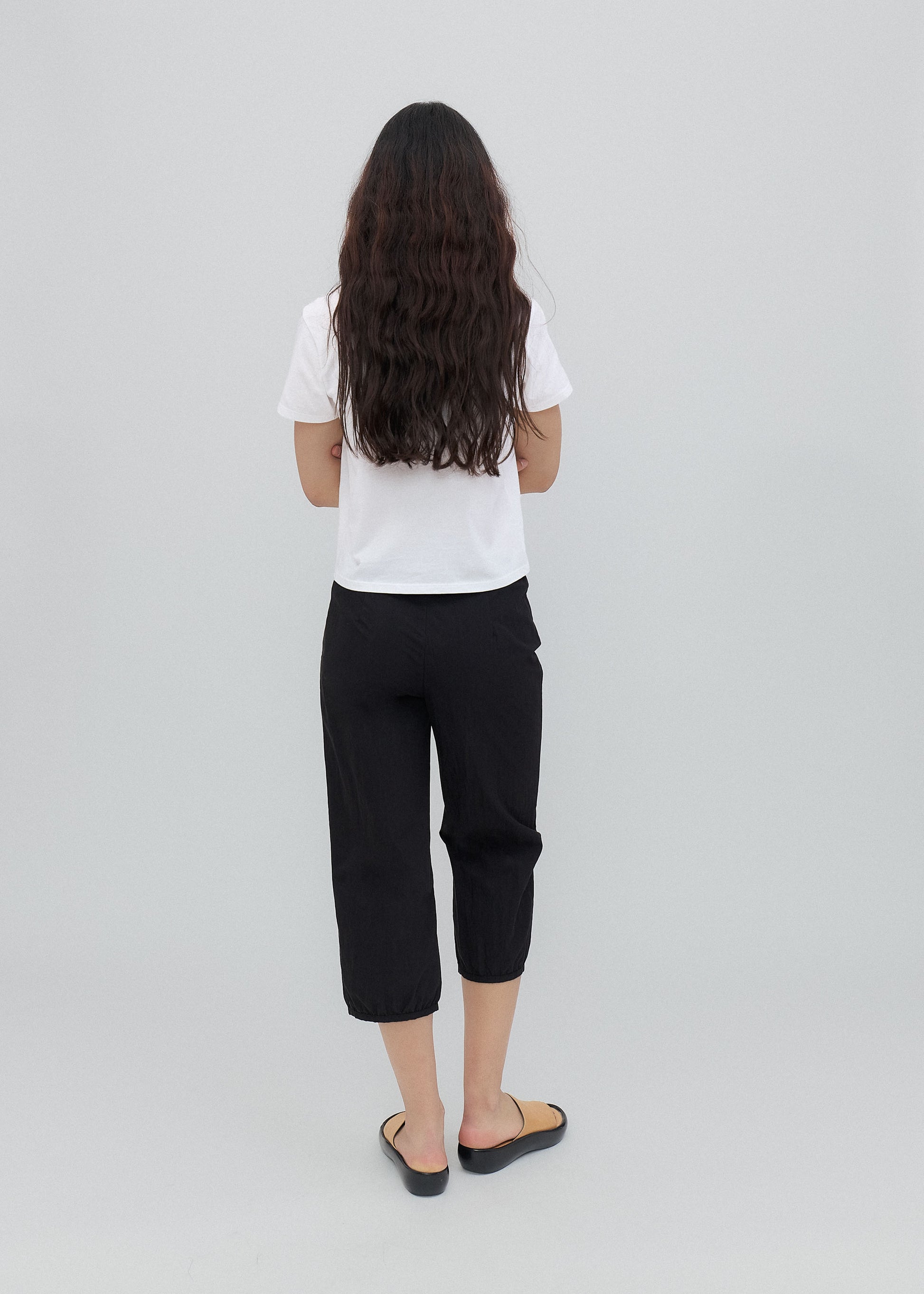 Person wearing a white shirt and black pants on a light gray background