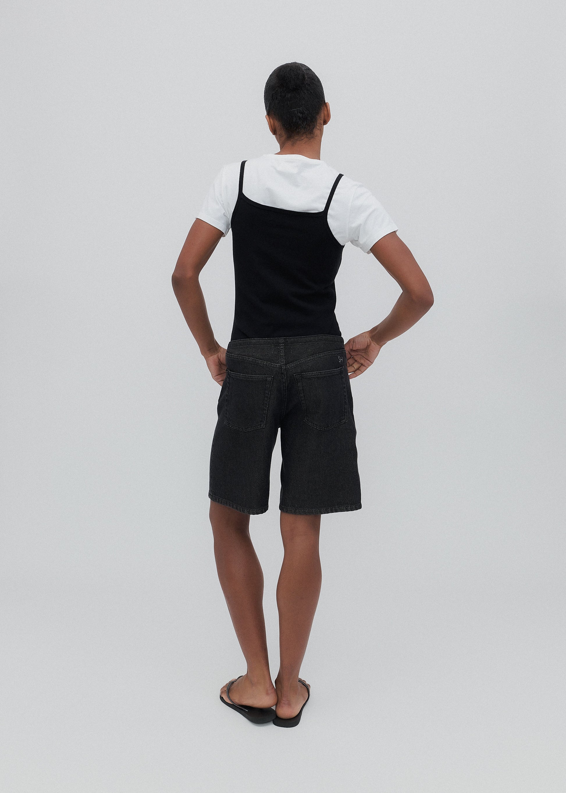 Person wearing a black pinafore over a white shirt on a plain background