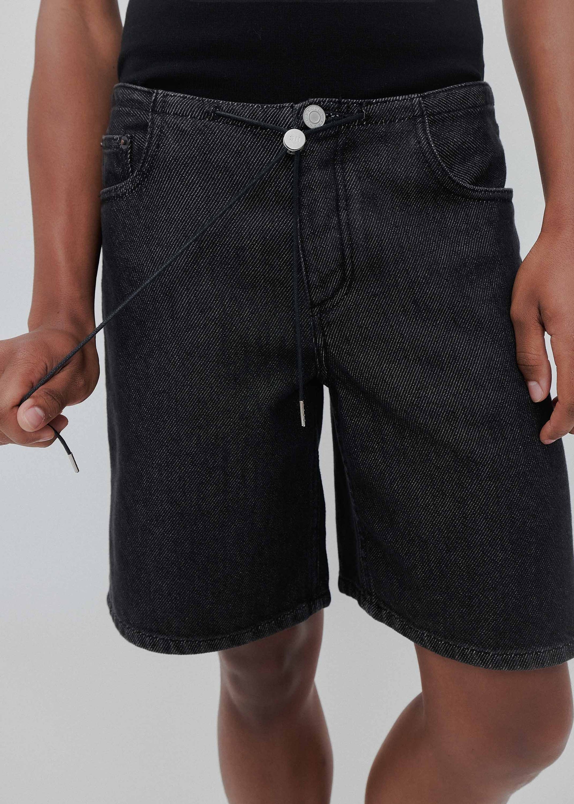 Black denim shorts worn by a person on a plain background