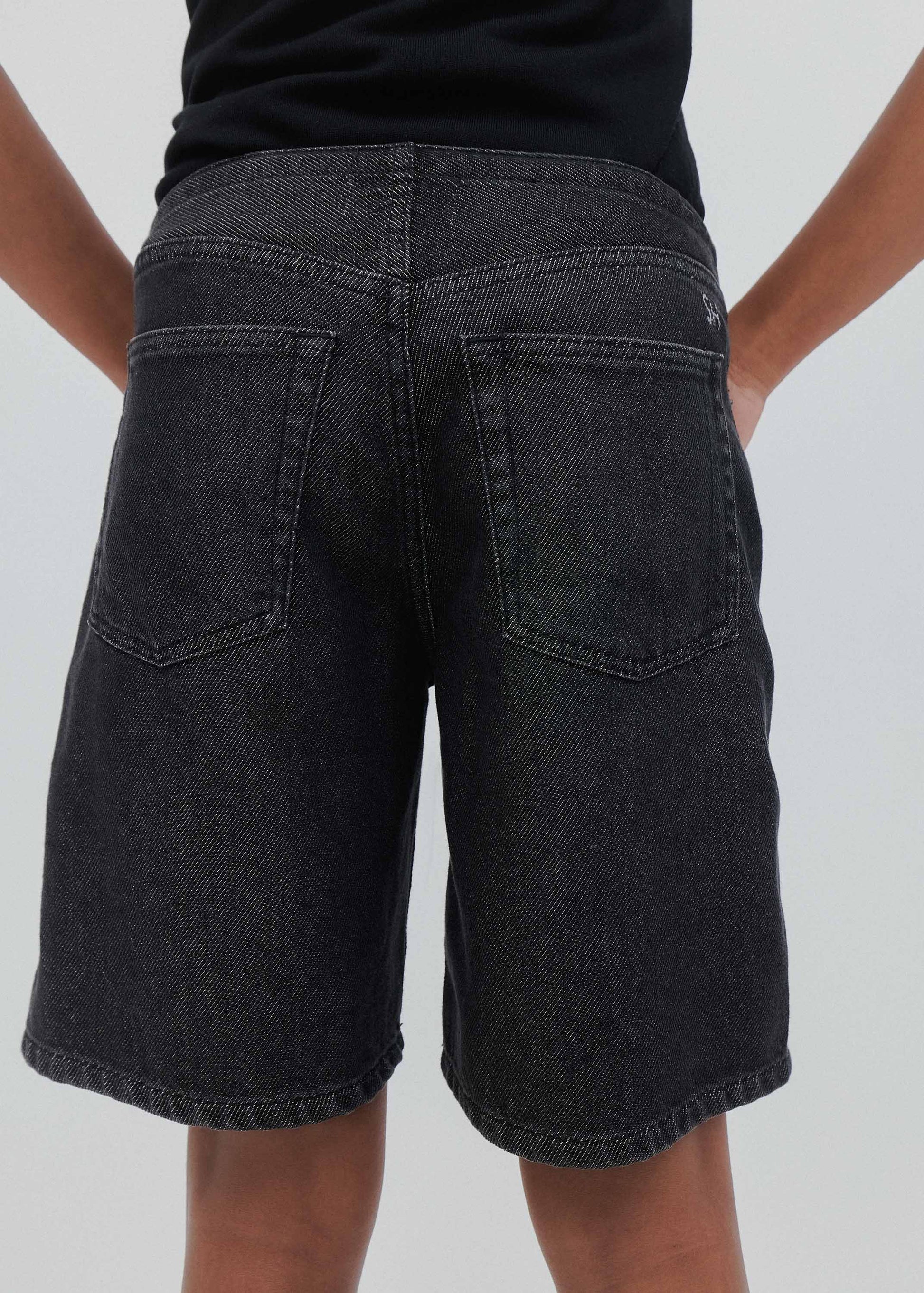 Black denim shorts worn by a person on a plain background