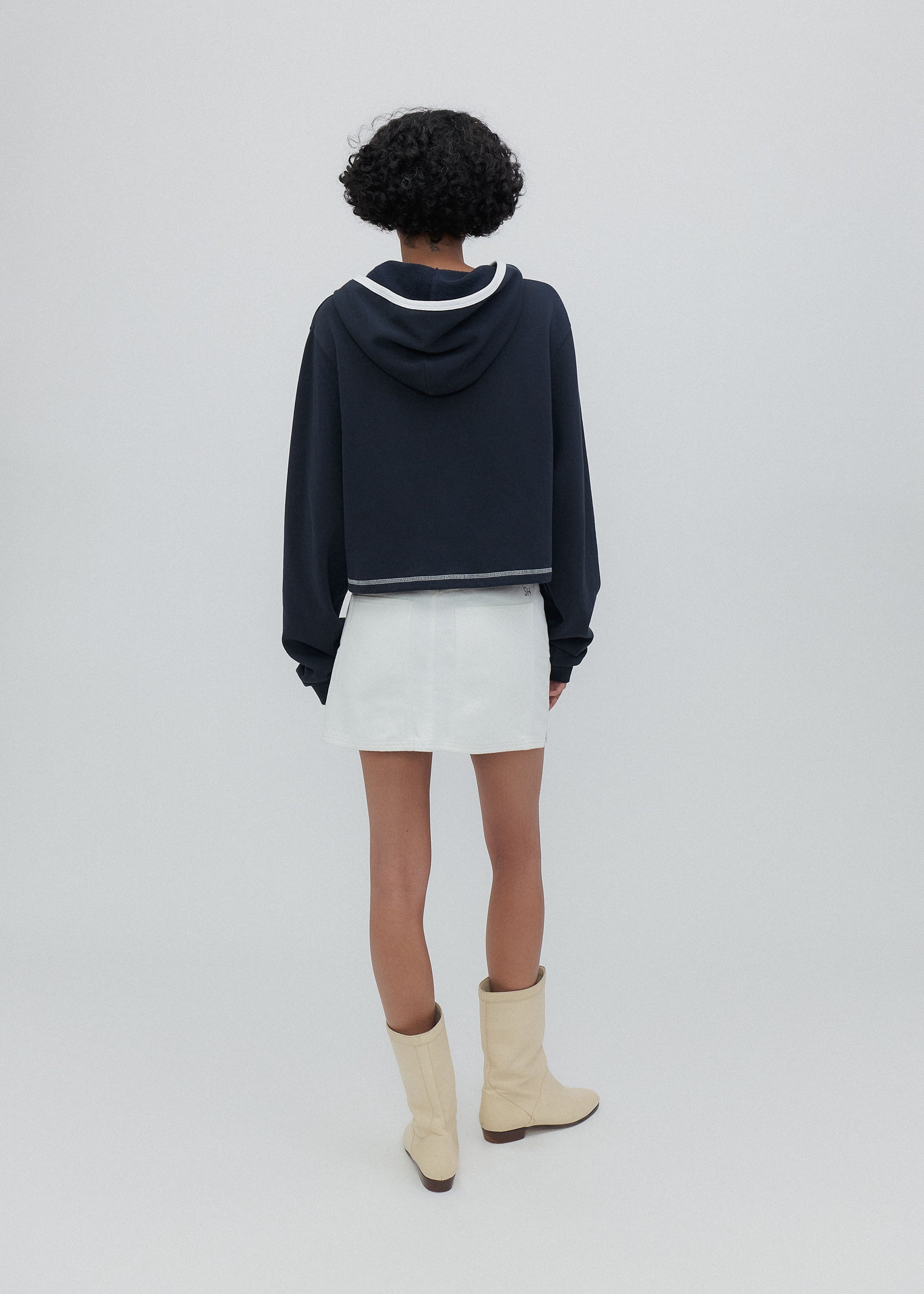 Person wearing a navy hoodie, white skirt, and beige boots on a light gray background