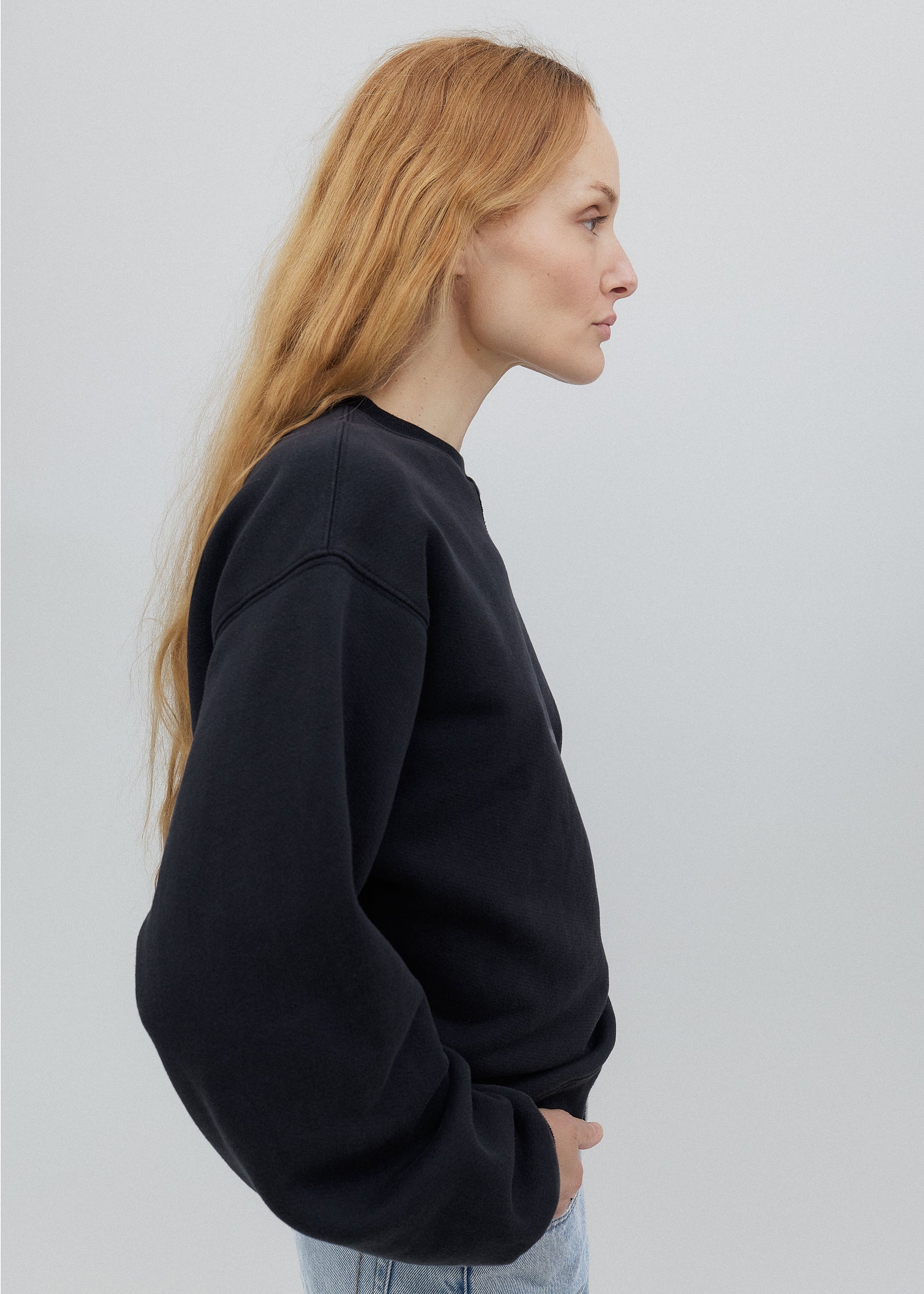 Person wearing a black sweater and light blue jeans on a white background