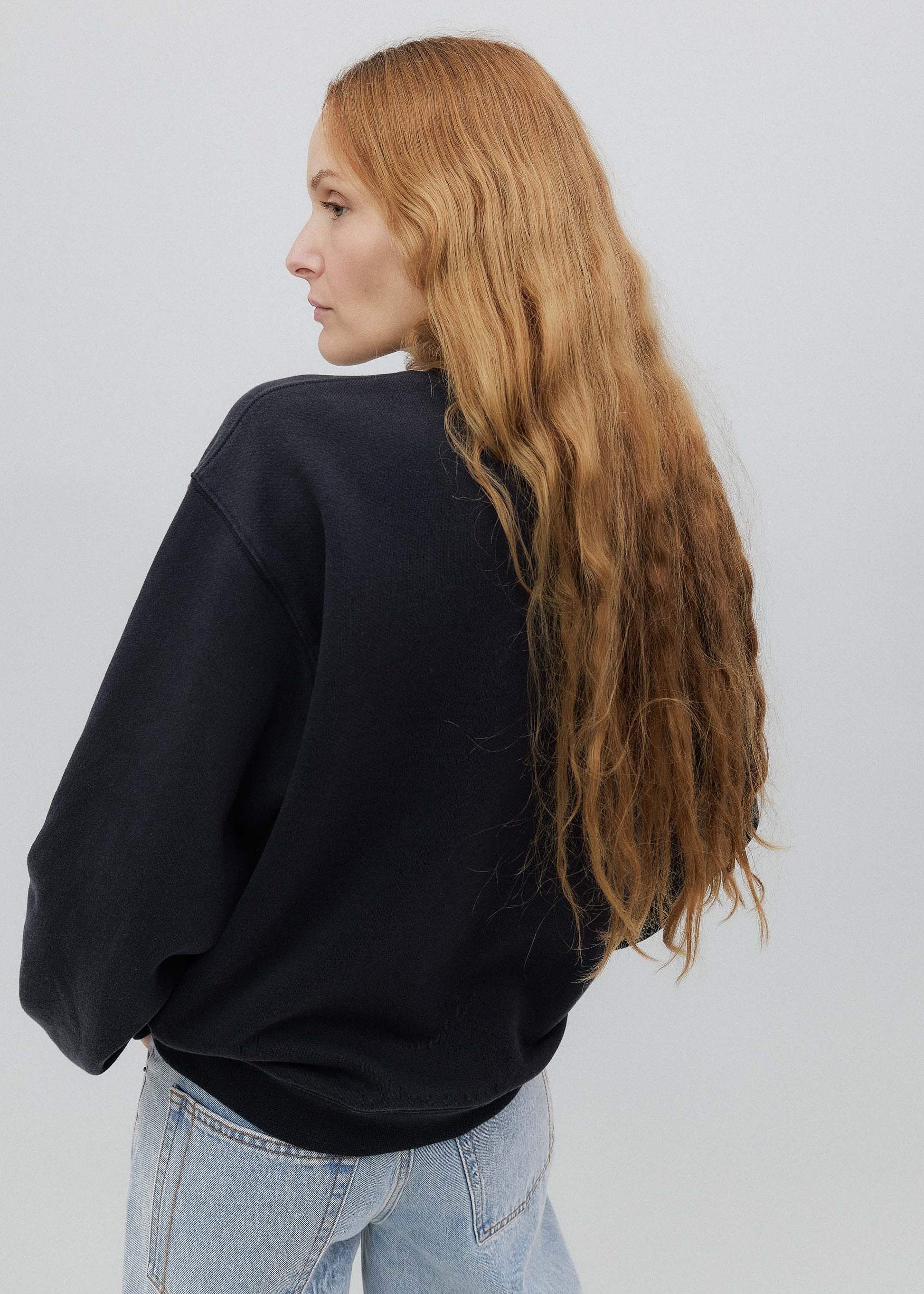 Person wearing a black sweater and light blue jeans on a white background