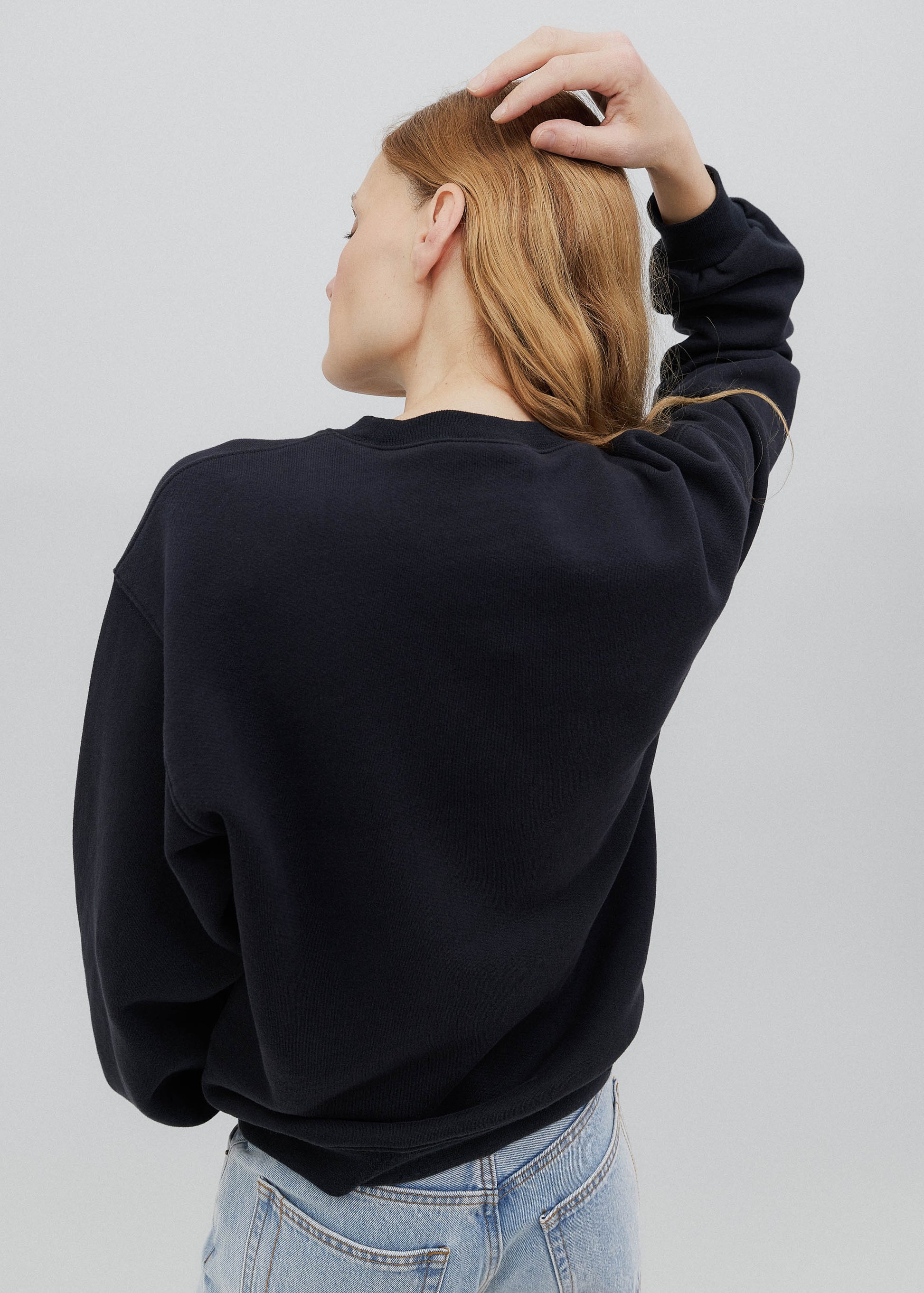 Person wearing a black sweater and light blue jeans on a white background