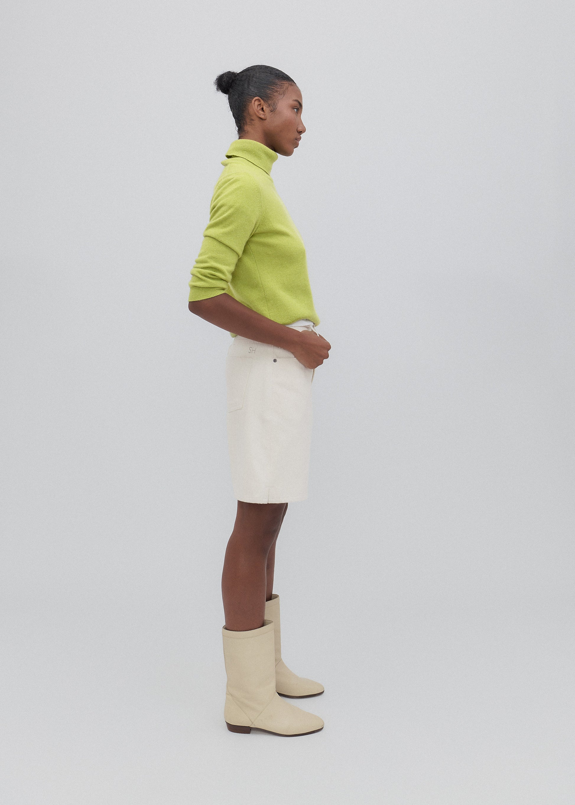 Person wearing a green sweater, white skirt, and cream boots on a light gray background
