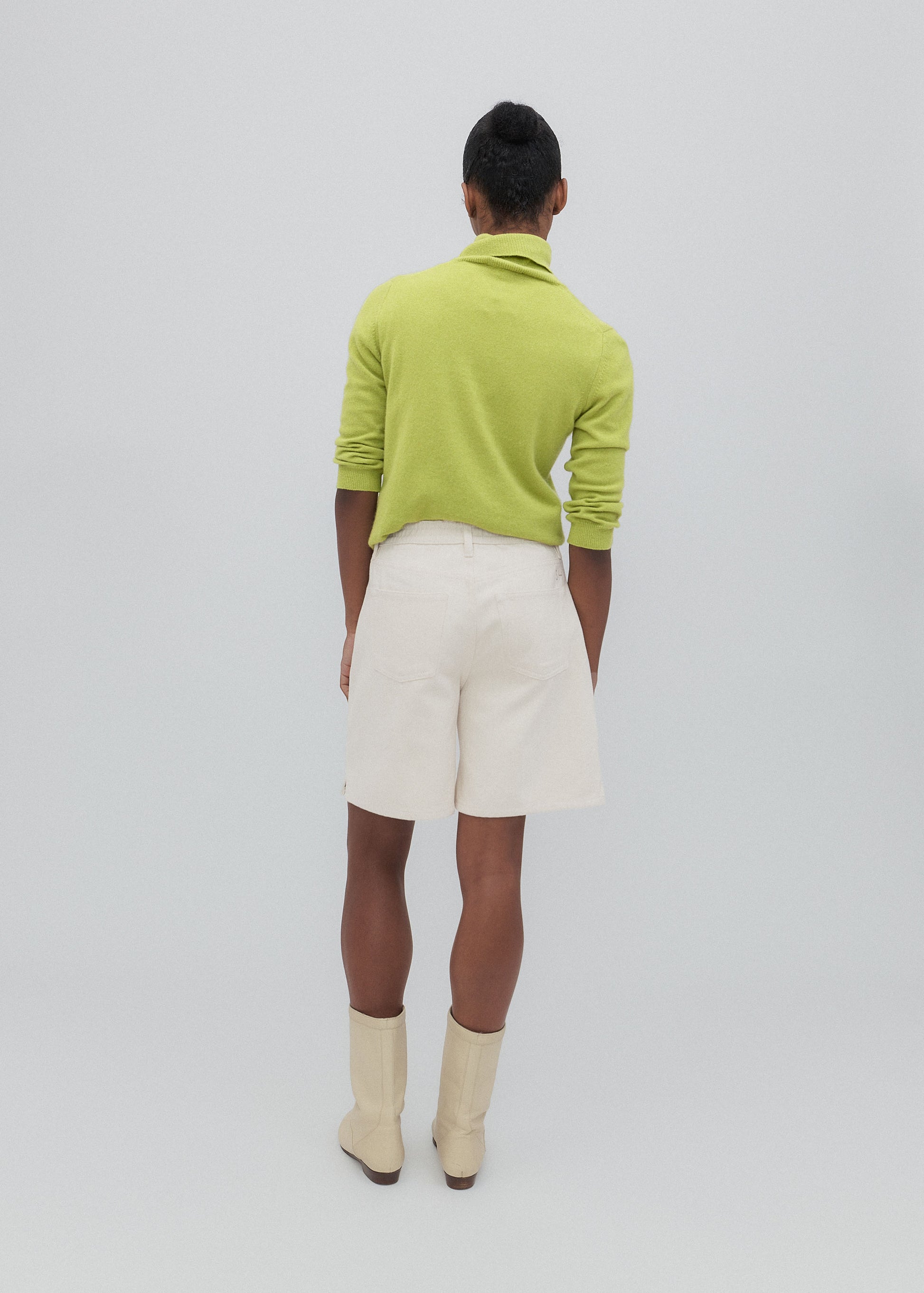 Person wearing a green sweater and white shorts on a plain background