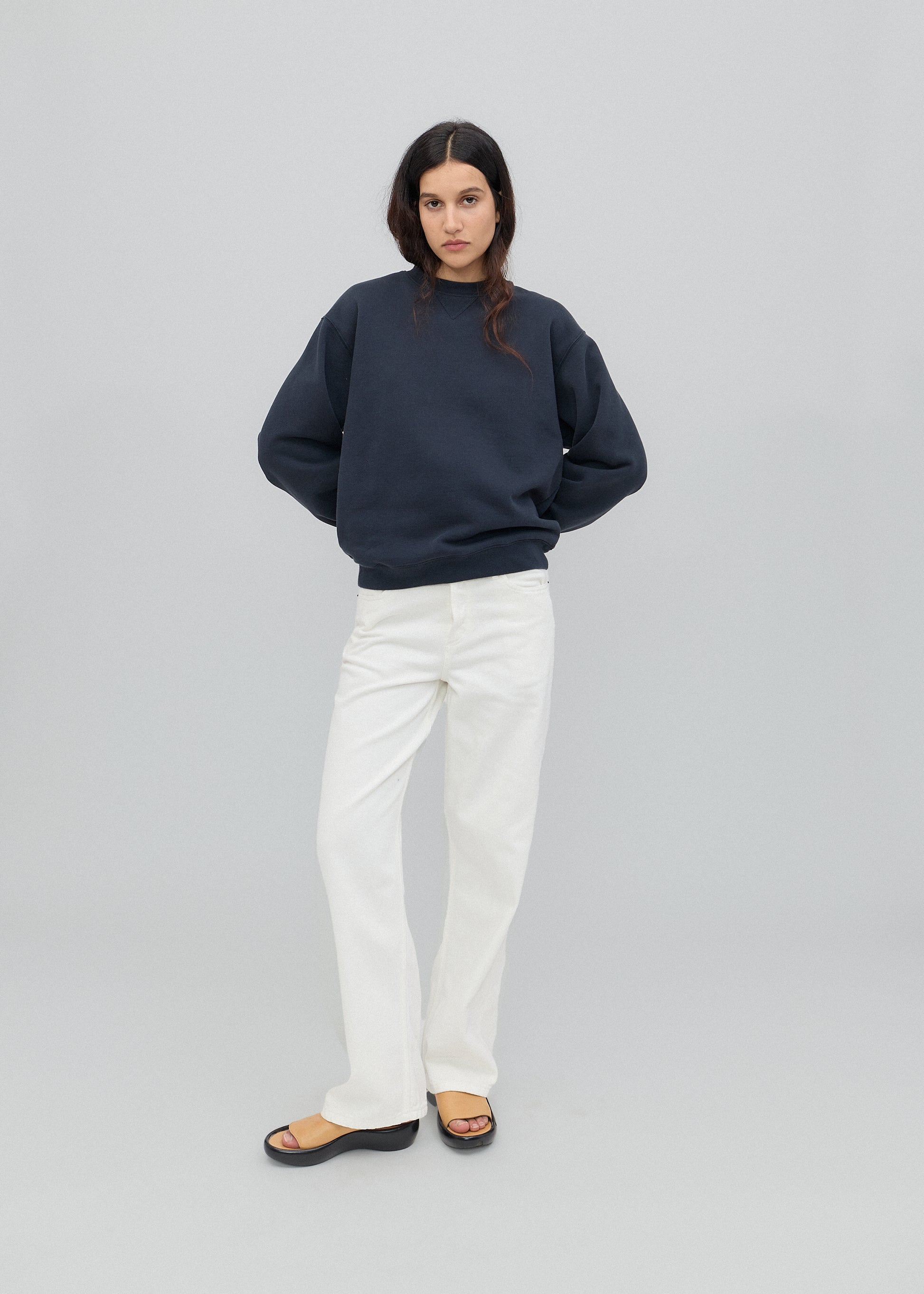 Person wearing a navy blue sweater and white jeans on a white background