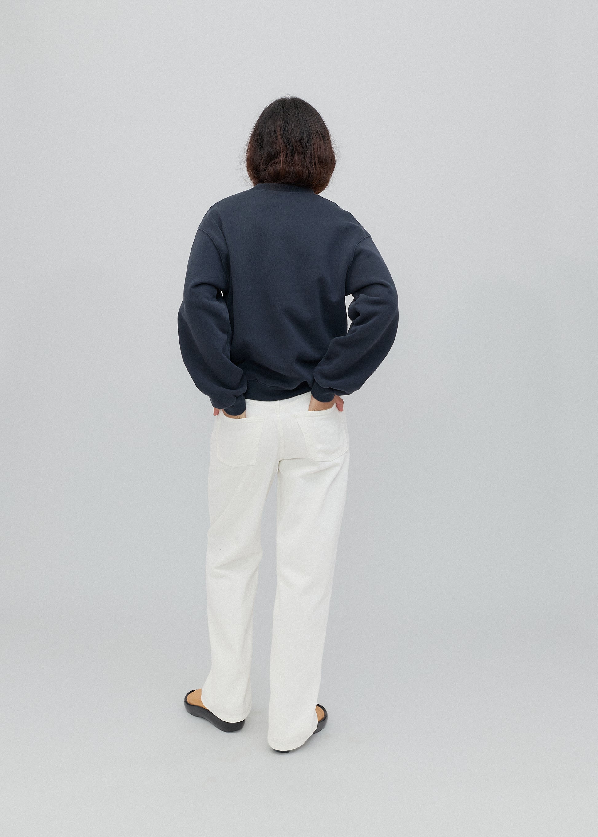 Person wearing a navy sweater and white pants on a light gray background