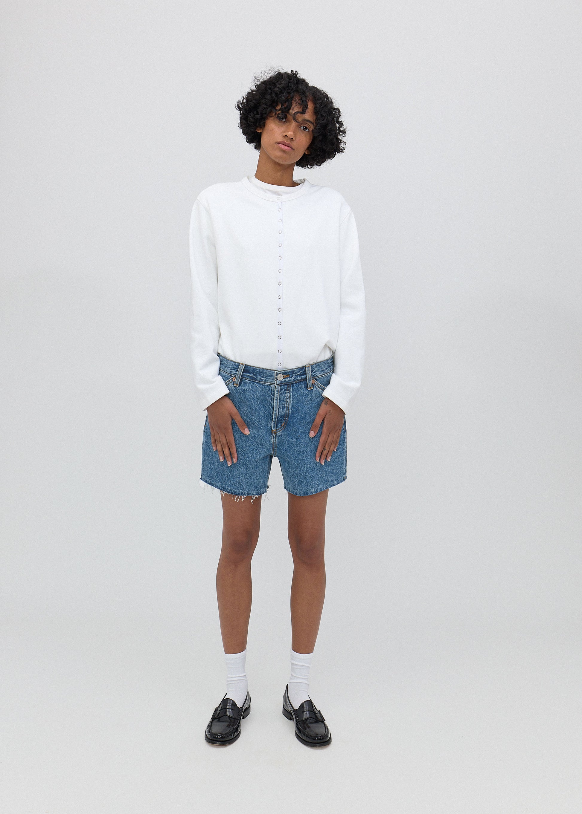Person wearing a white sweater, blue denim shorts, and black shoes on a white background