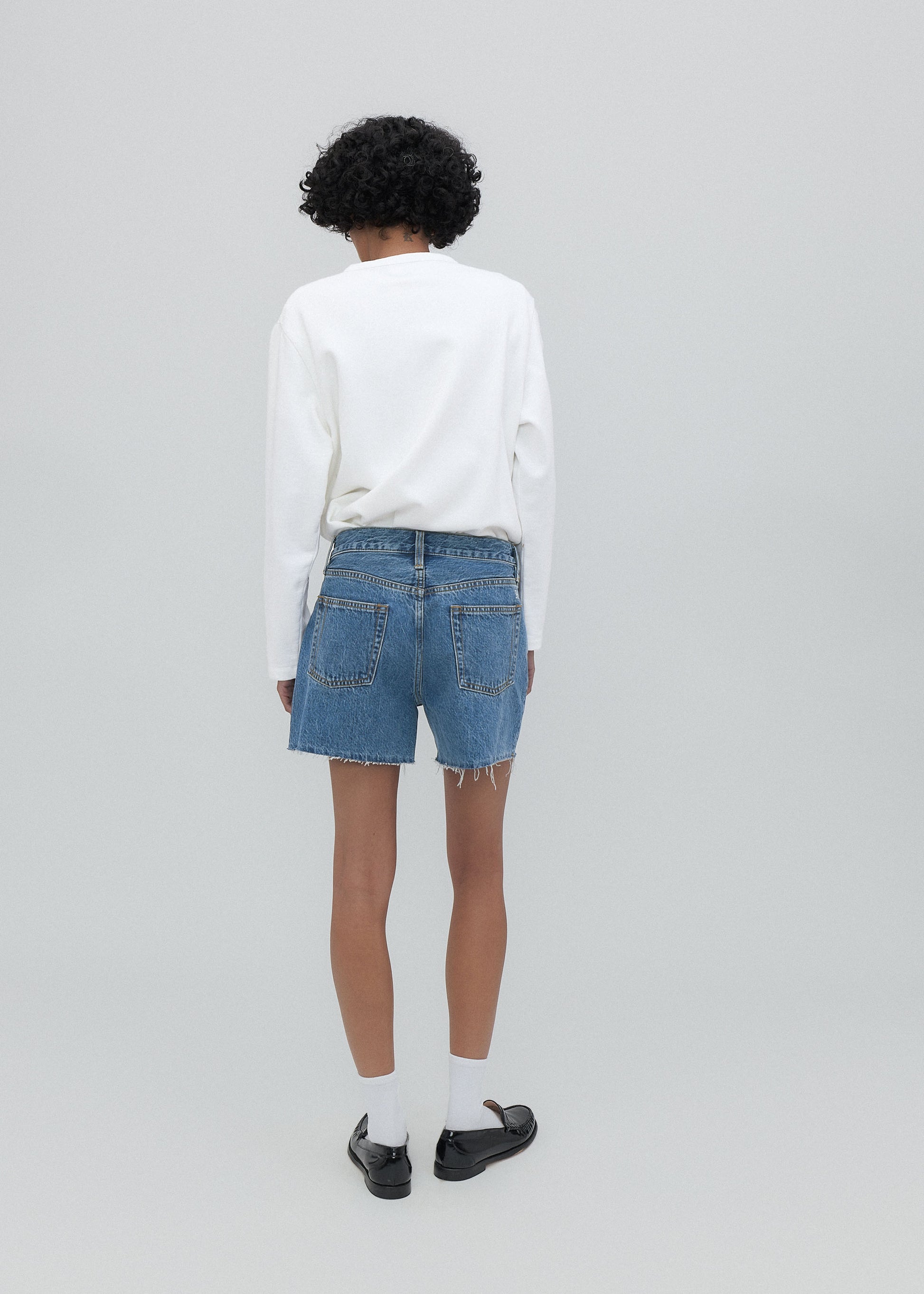 Person wearing a white sweatshirt and blue denim shorts on a plain background