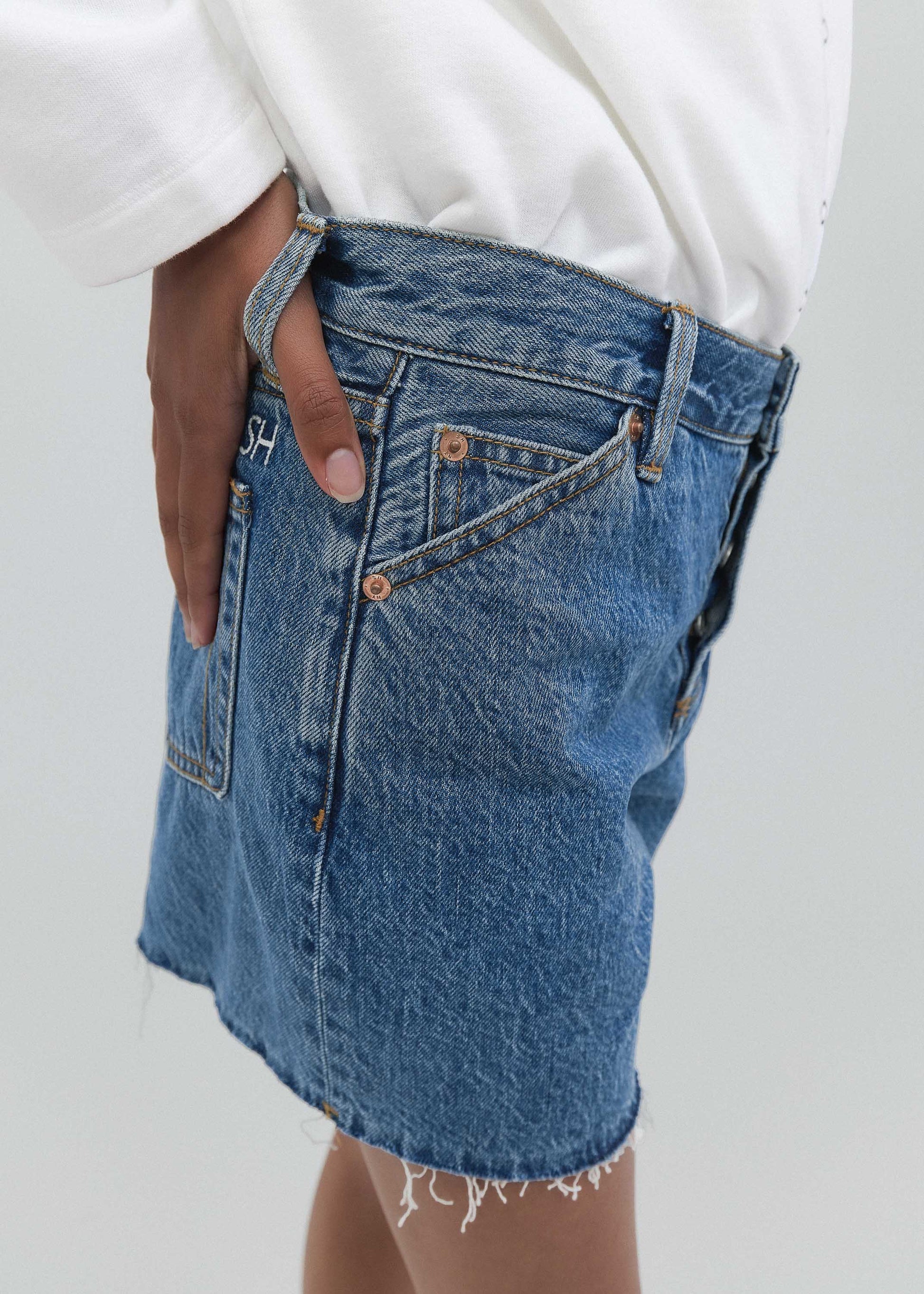 Blue denim skirt worn with a white top on a plain background