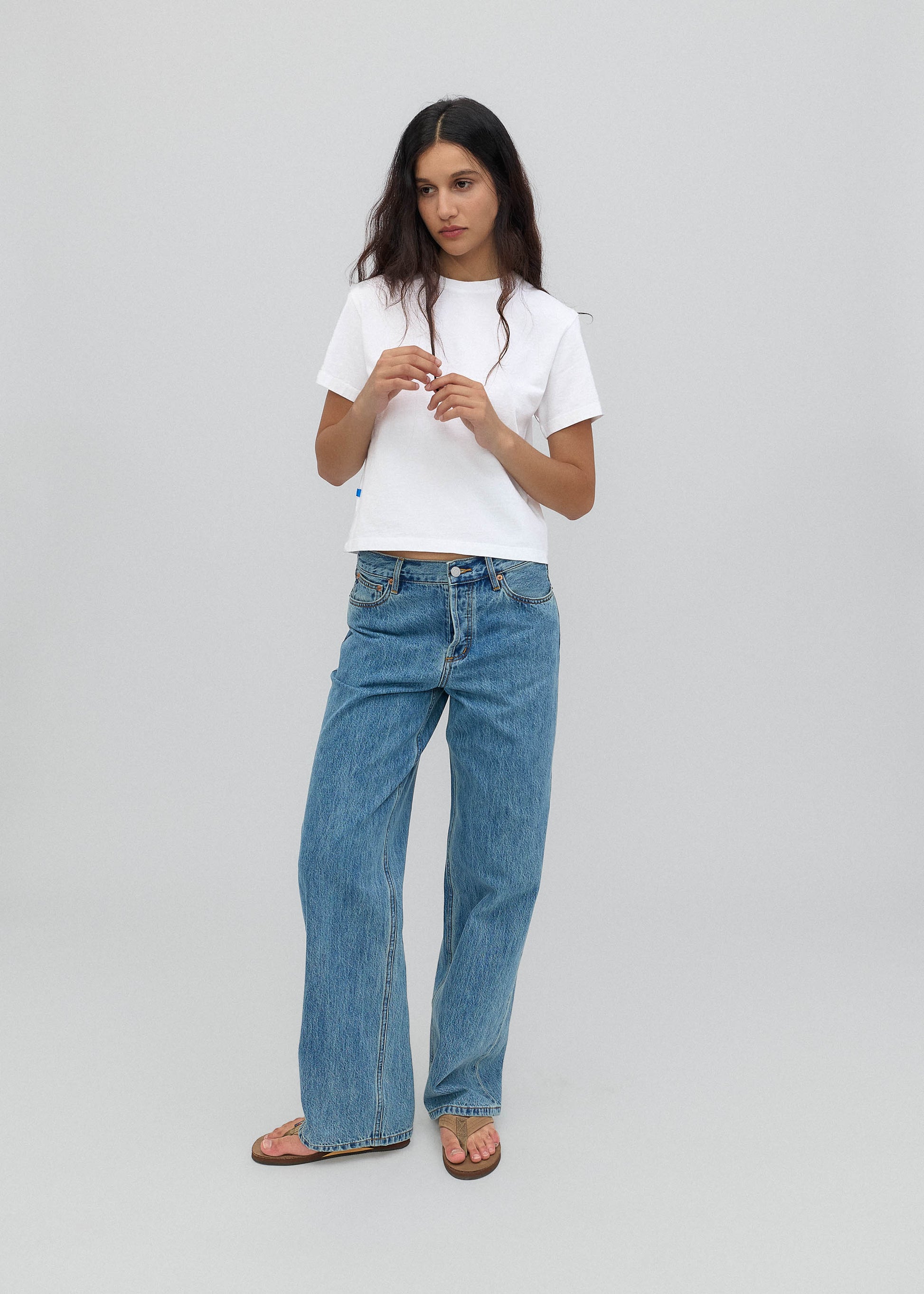 Woman wearing a white t-shirt and blue jeans on a gray background
