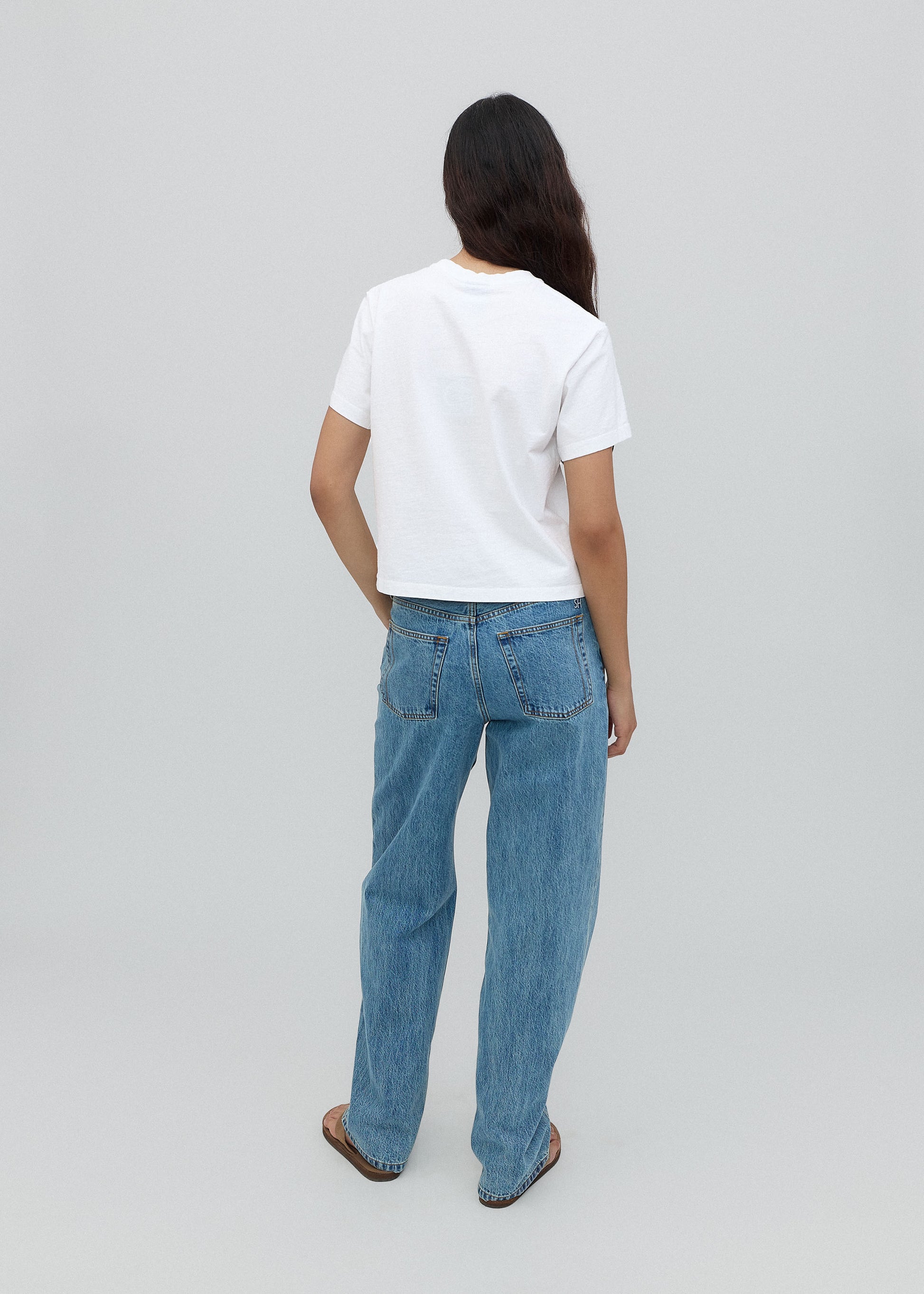 Person wearing a white t-shirt and blue jeans on a plain background