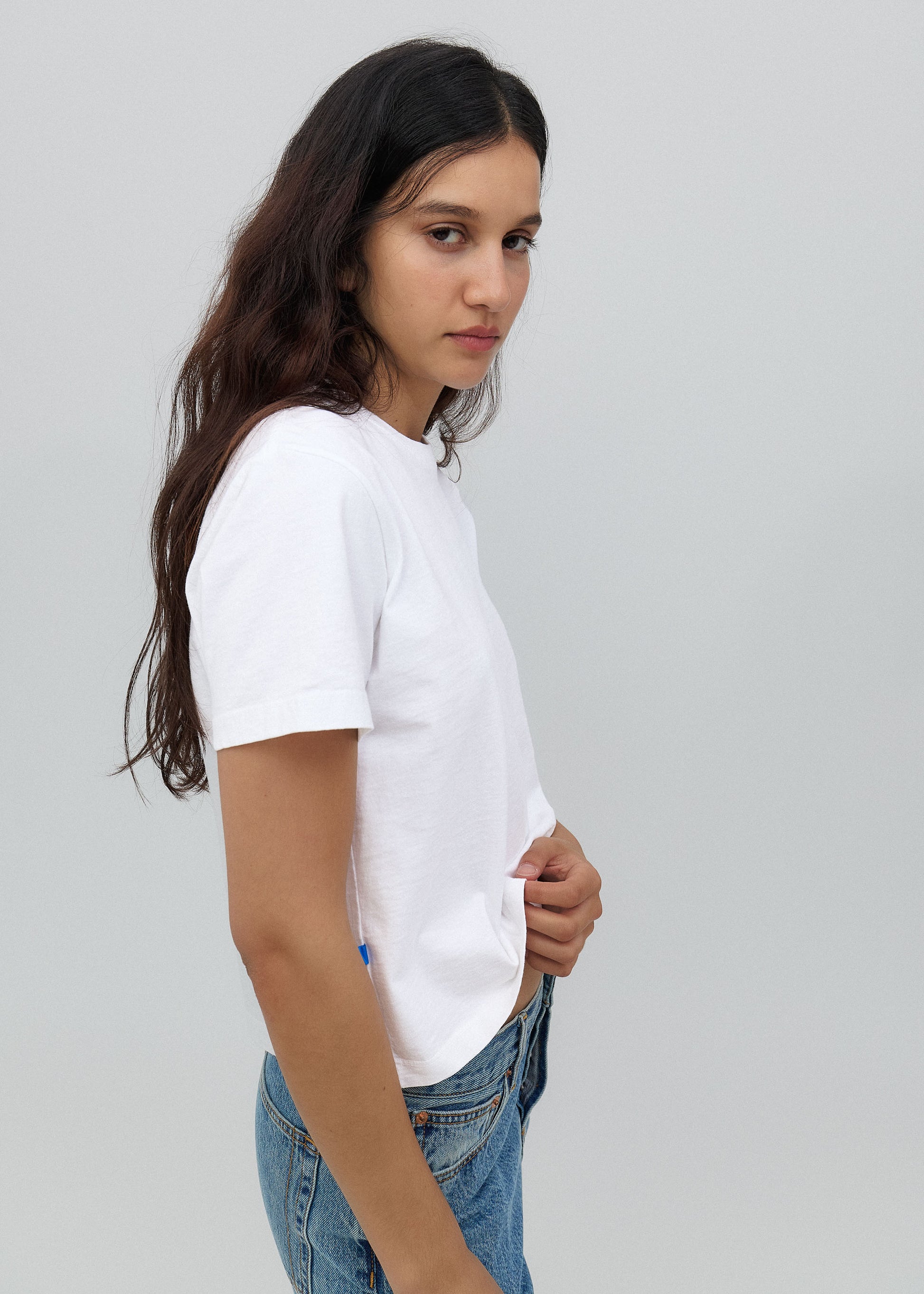 Person wearing a white t-shirt and blue jeans on a plain background