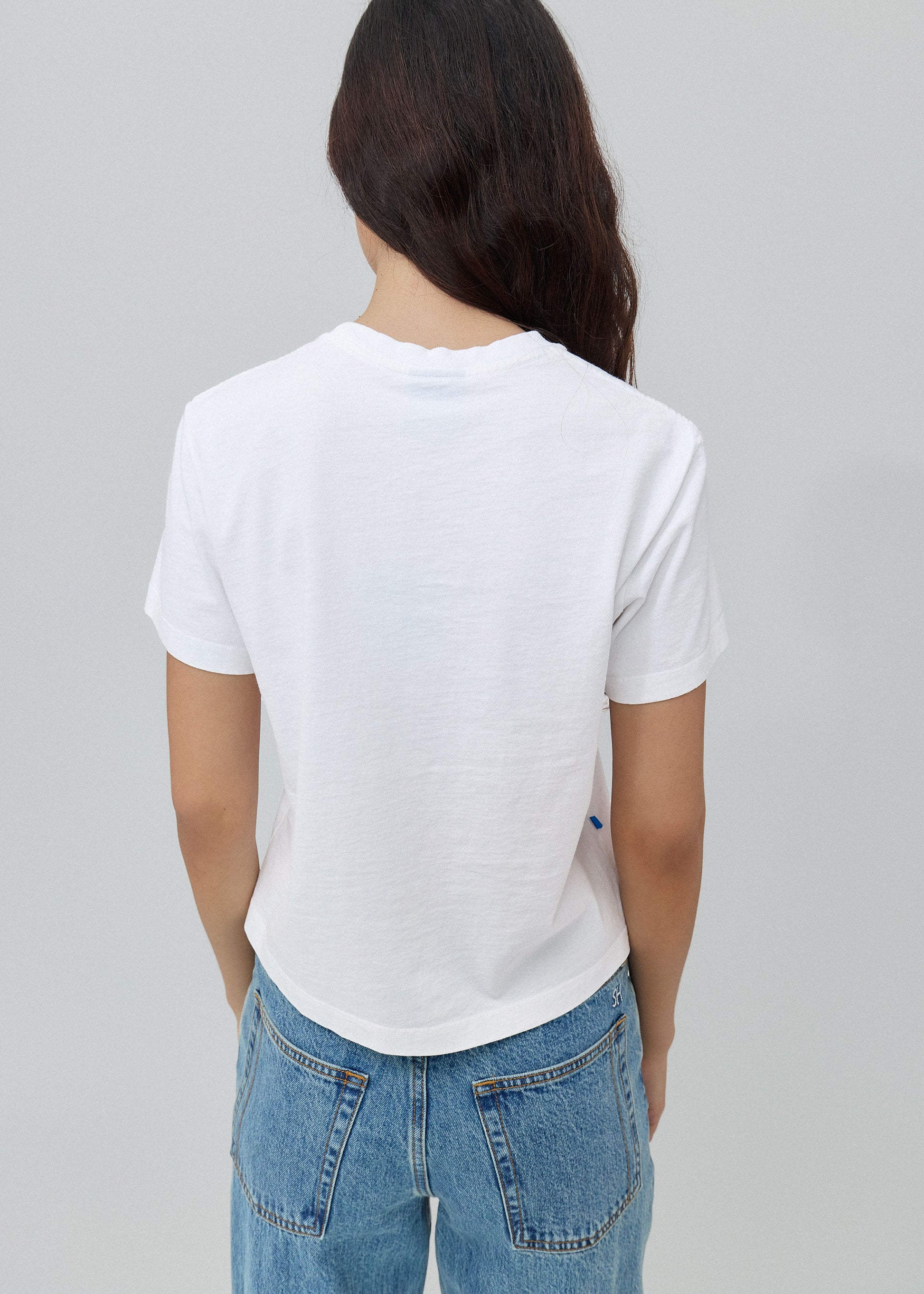 Person wearing a white t-shirt and blue jeans on a gray background