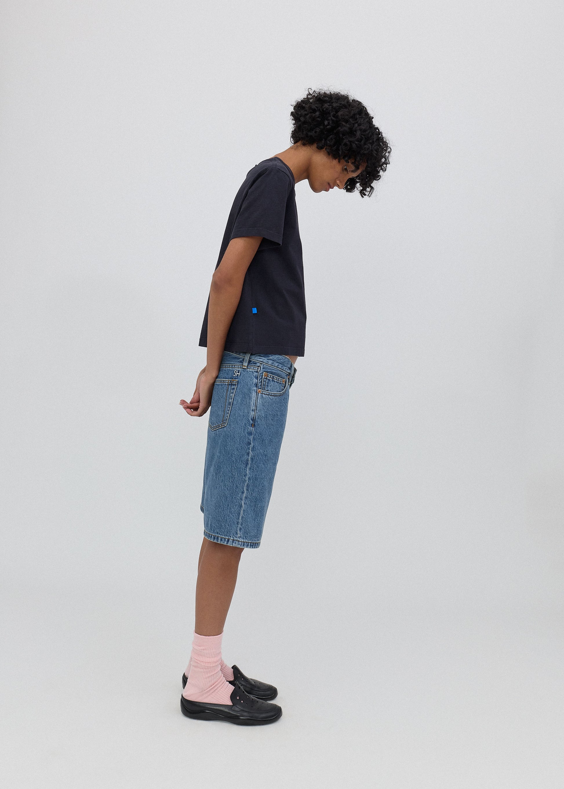 Person wearing a black t-shirt, blue denim shorts, and pink socks on a white background