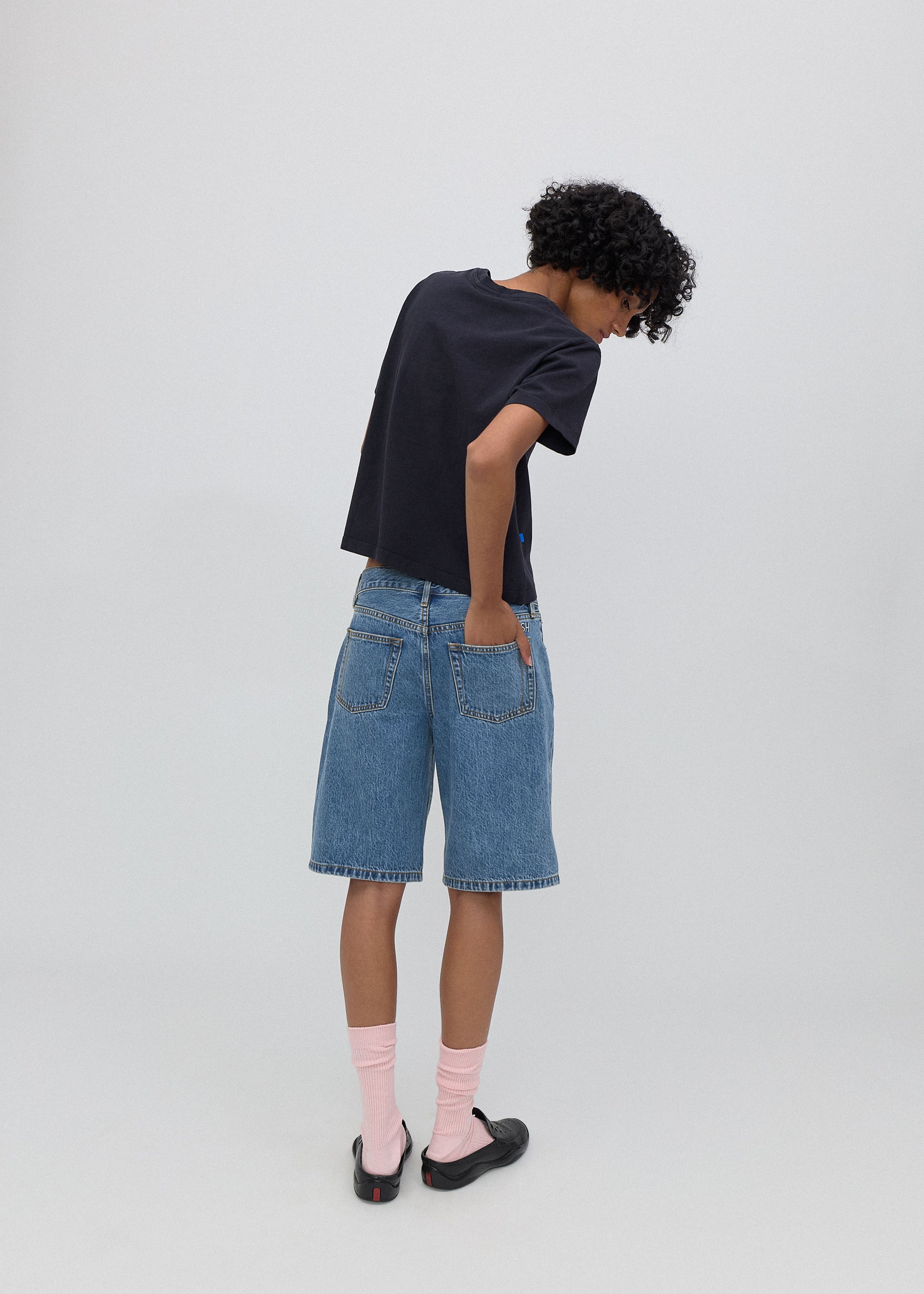 Person wearing a black t-shirt and blue denim shorts on a white background